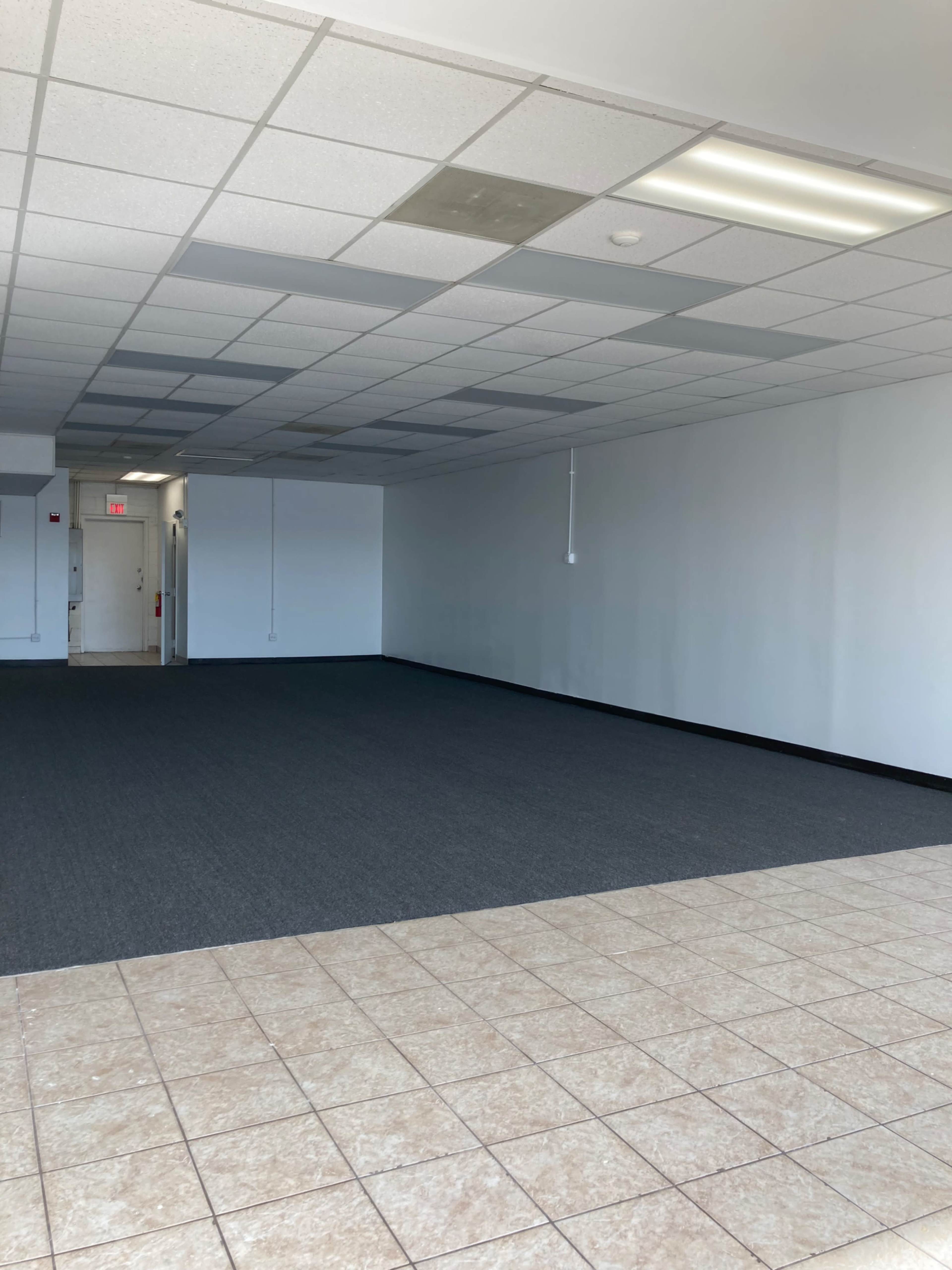 A vacant interior space with tiled flooring and wall-to-wall carpeting.
