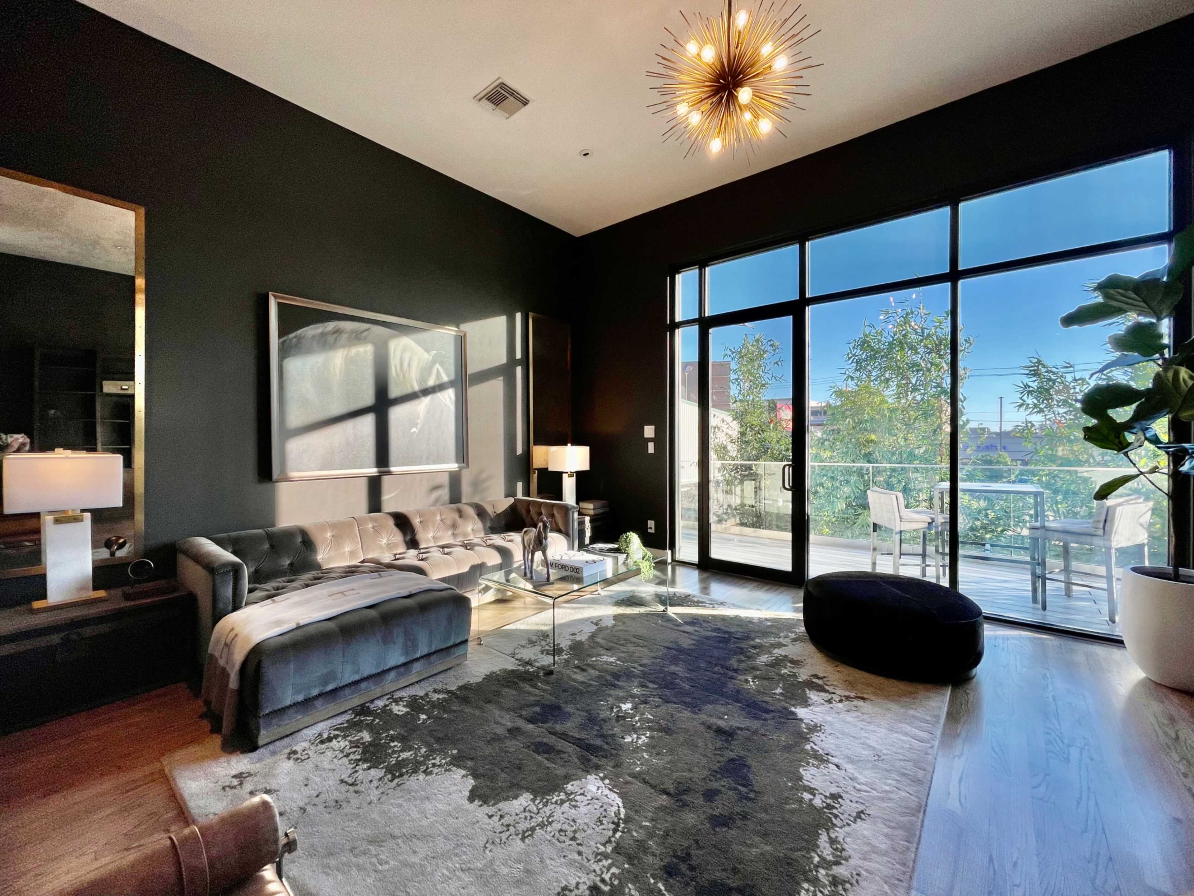 A modern living room features a velvet sofa, a glass coffee table, and large windows allowing natural light to illuminate the space.