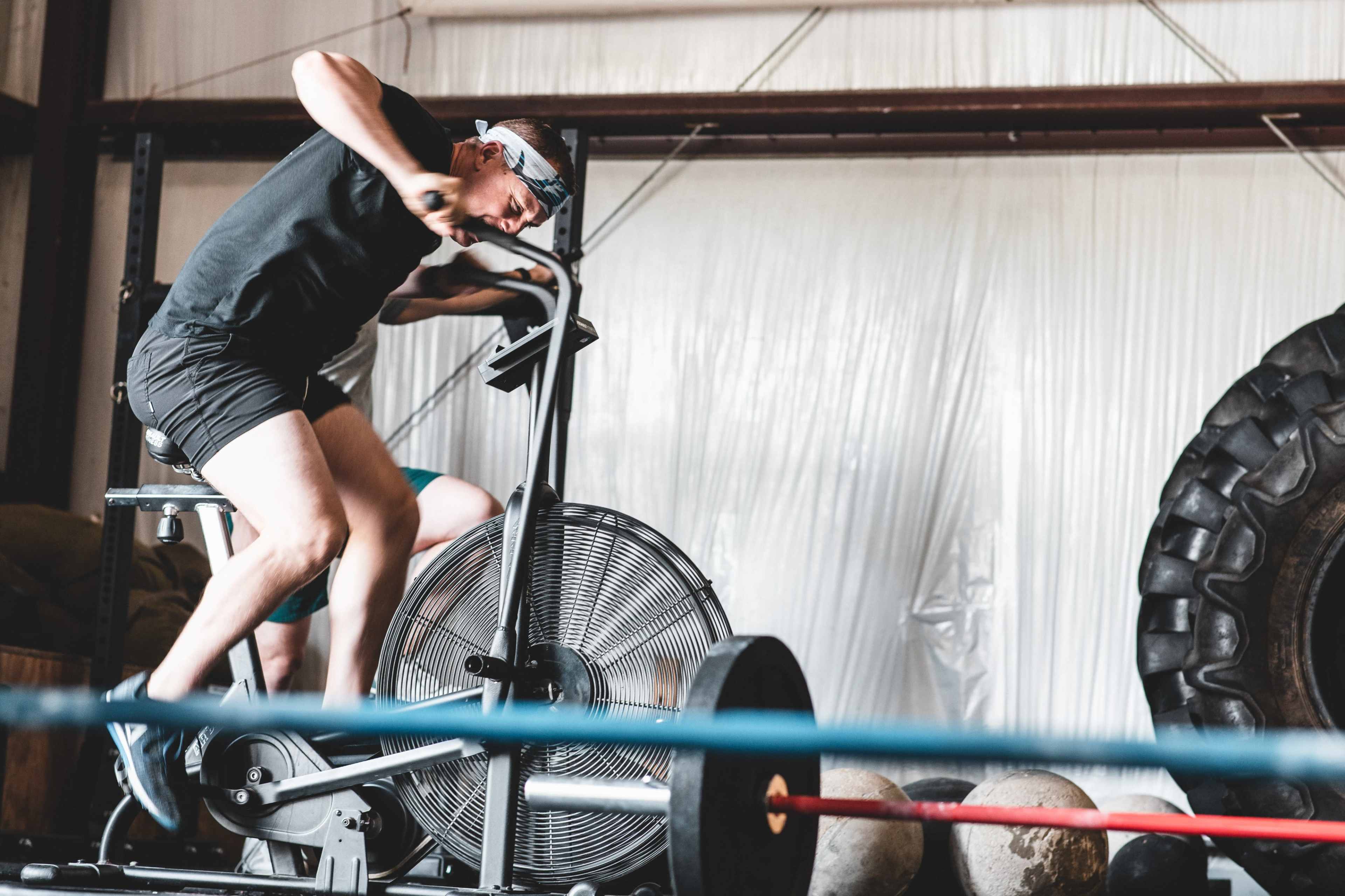 A person is vigorously exercising on a stationary air bike in a gym setting.