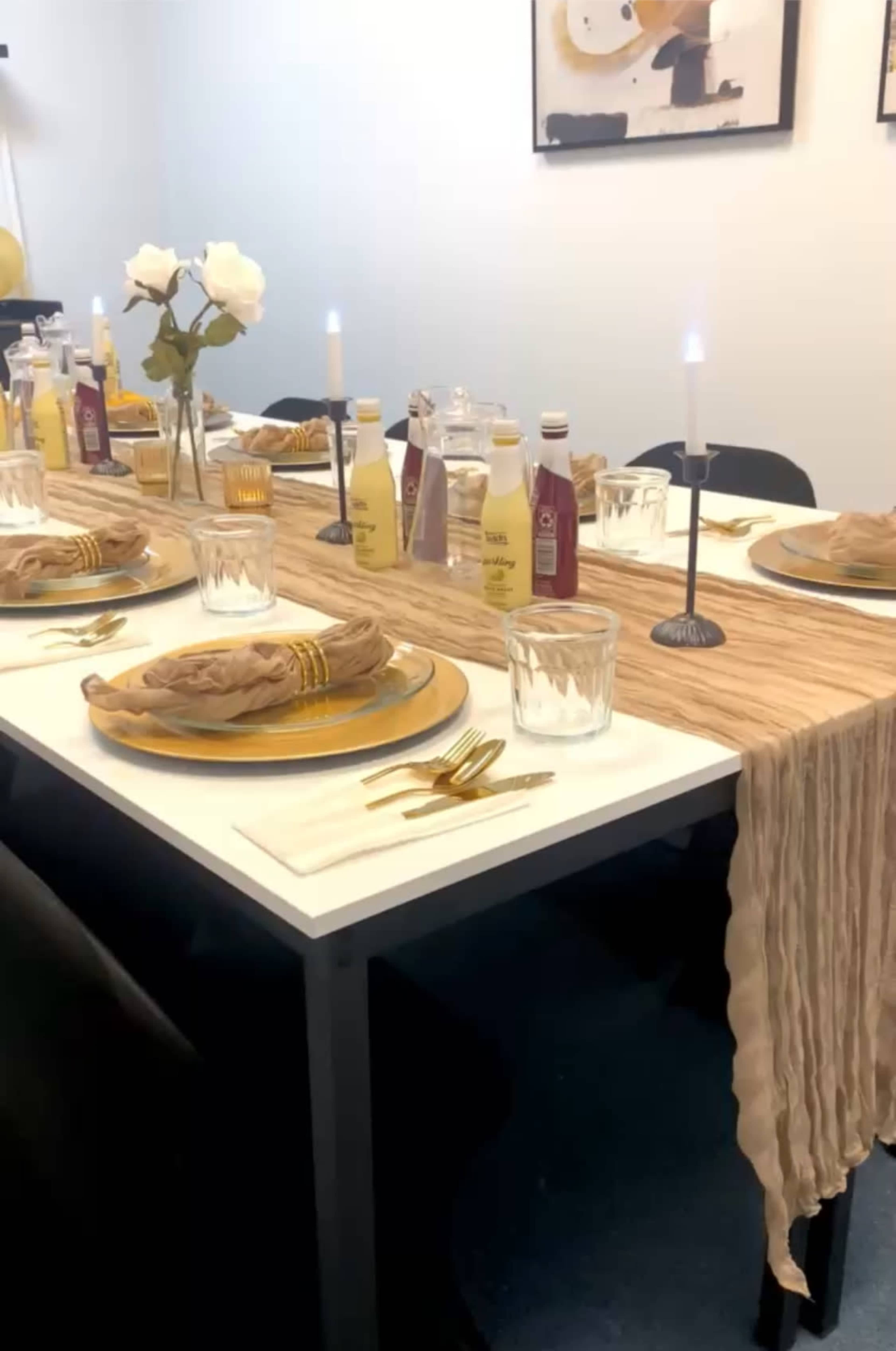 A dining table is set with plates, glasses, and utensils, adorned with a beige table runner and a vase of flowers.