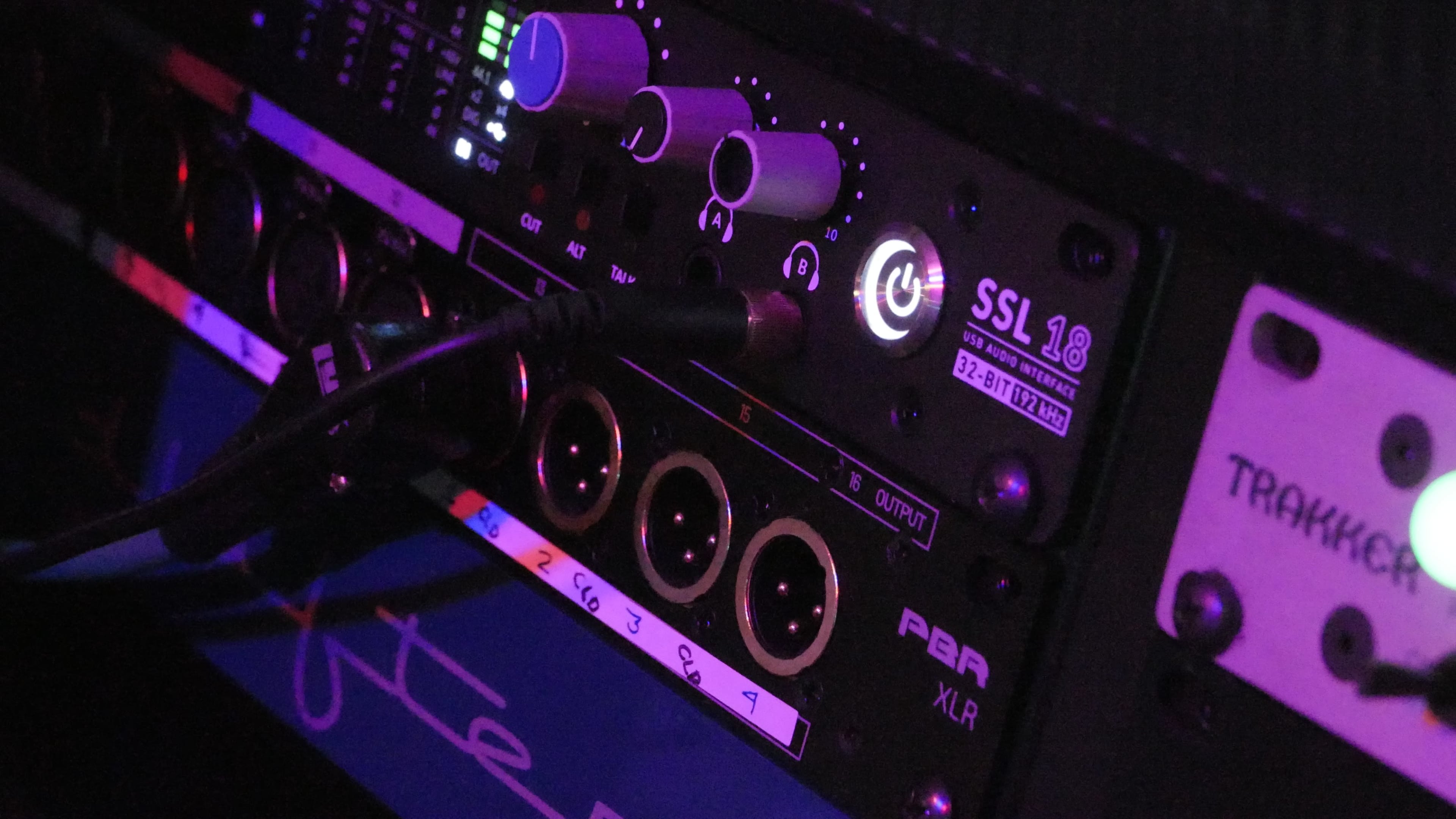 The image shows a close-up of audio equipment, featuring various knobs, buttons, and input/output ports on a mixing console.