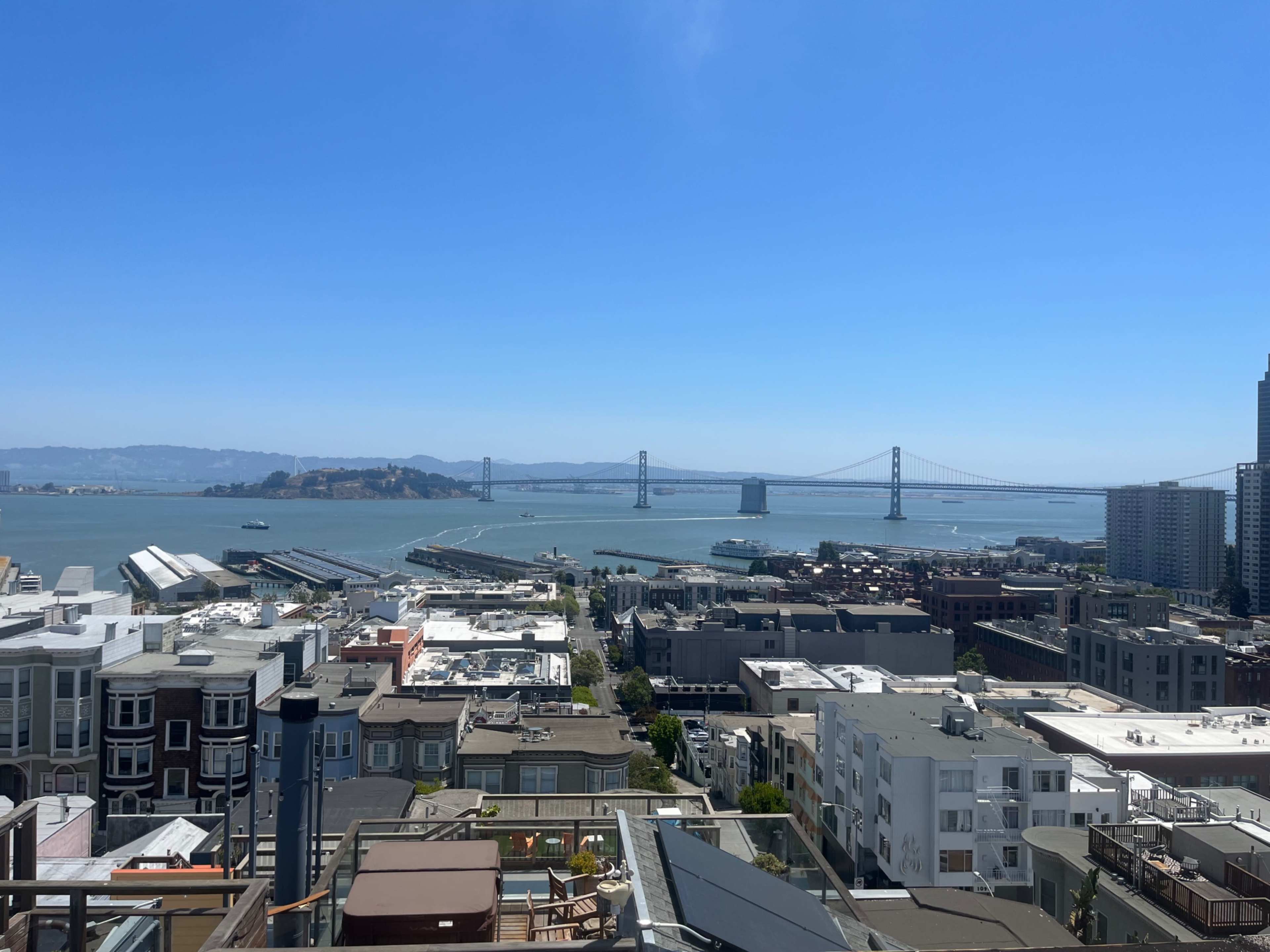 A panoramic view of San Francisco Bay, featuring the Bay Bridge in the distance and a cluster of buildings in the foreground.