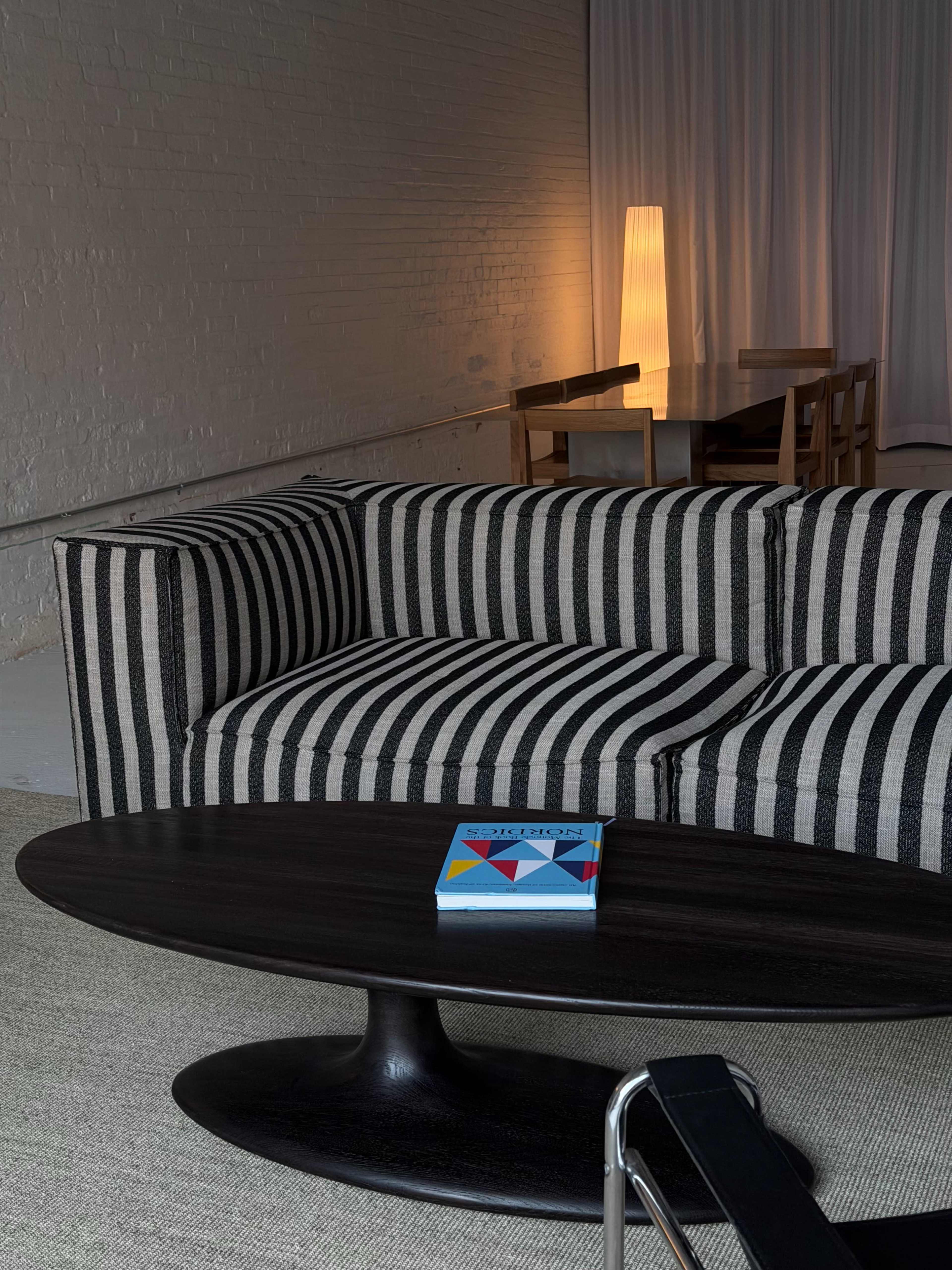 A striped couch faces a round coffee table with a colorful book on it, while a softly lit lamp is visible in the background.