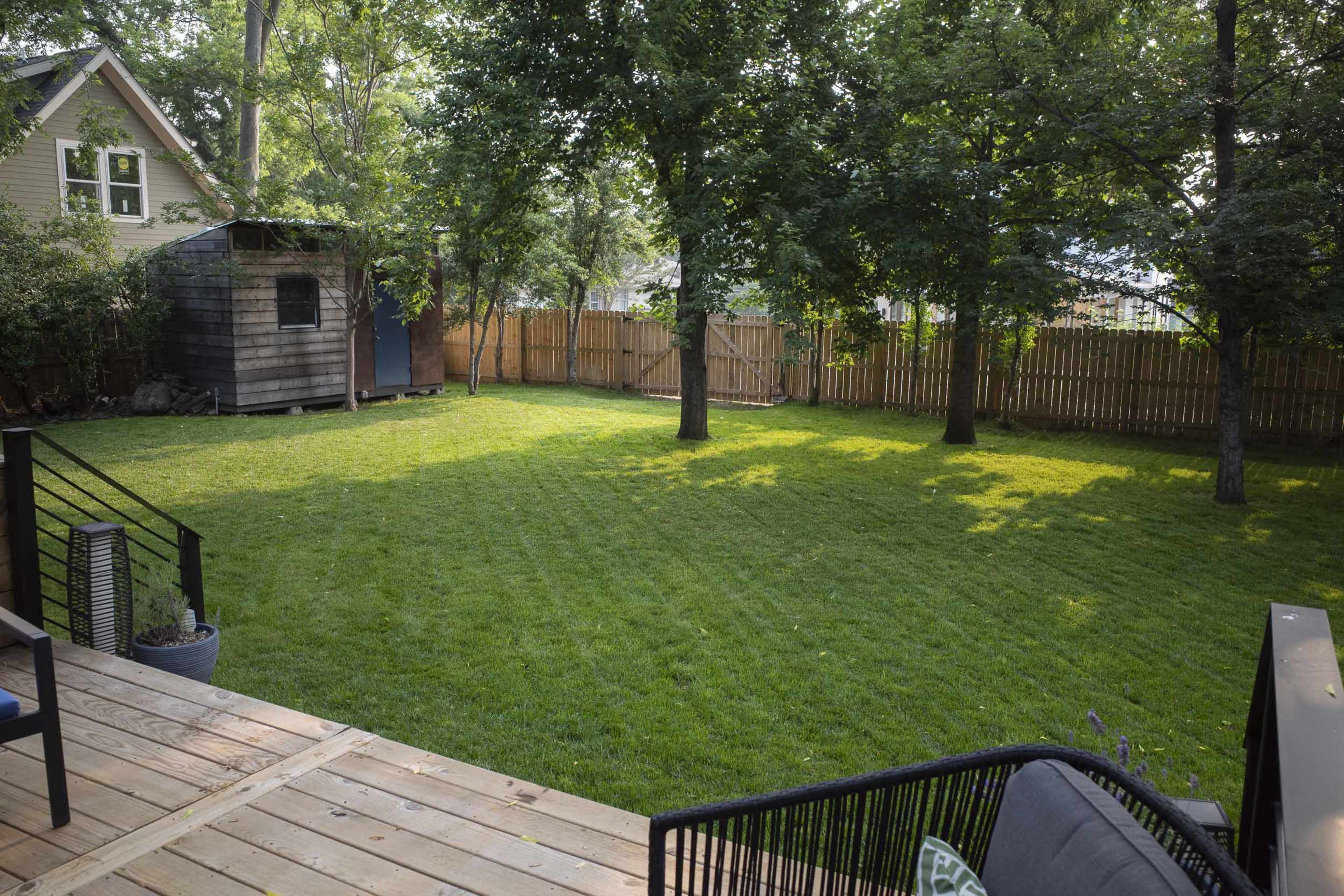 A well-maintained backyard with a neatly manicured lawn, a small shed, and trees providing shade.
