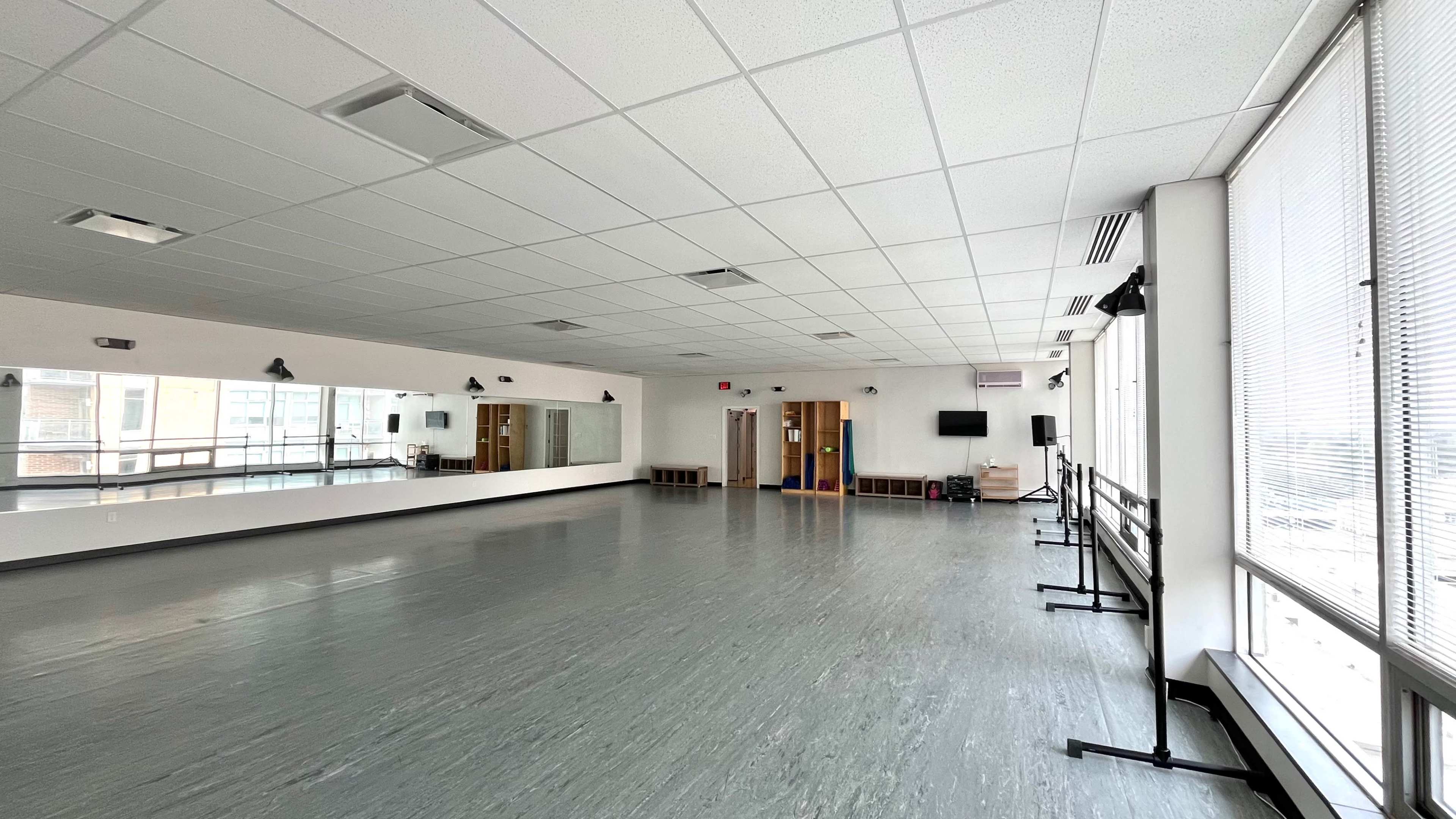 A spacious dance studio with mirrors on one wall, wooden ballet bars, and large windows providing natural light.
