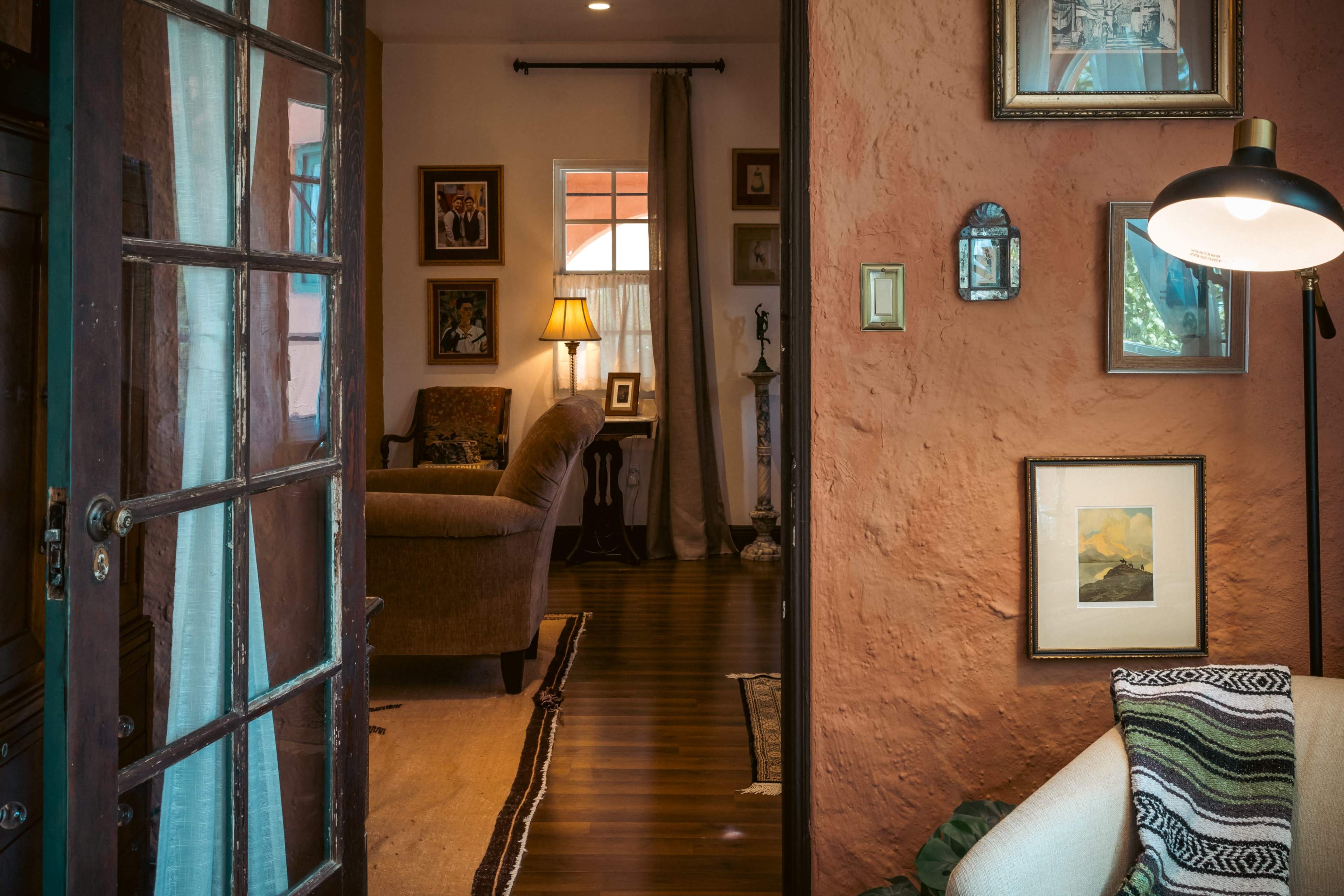 A cozy interior view of a living space, featuring a doorway with a glass panel, framed artwork on the walls, and a sofa in the foreground.