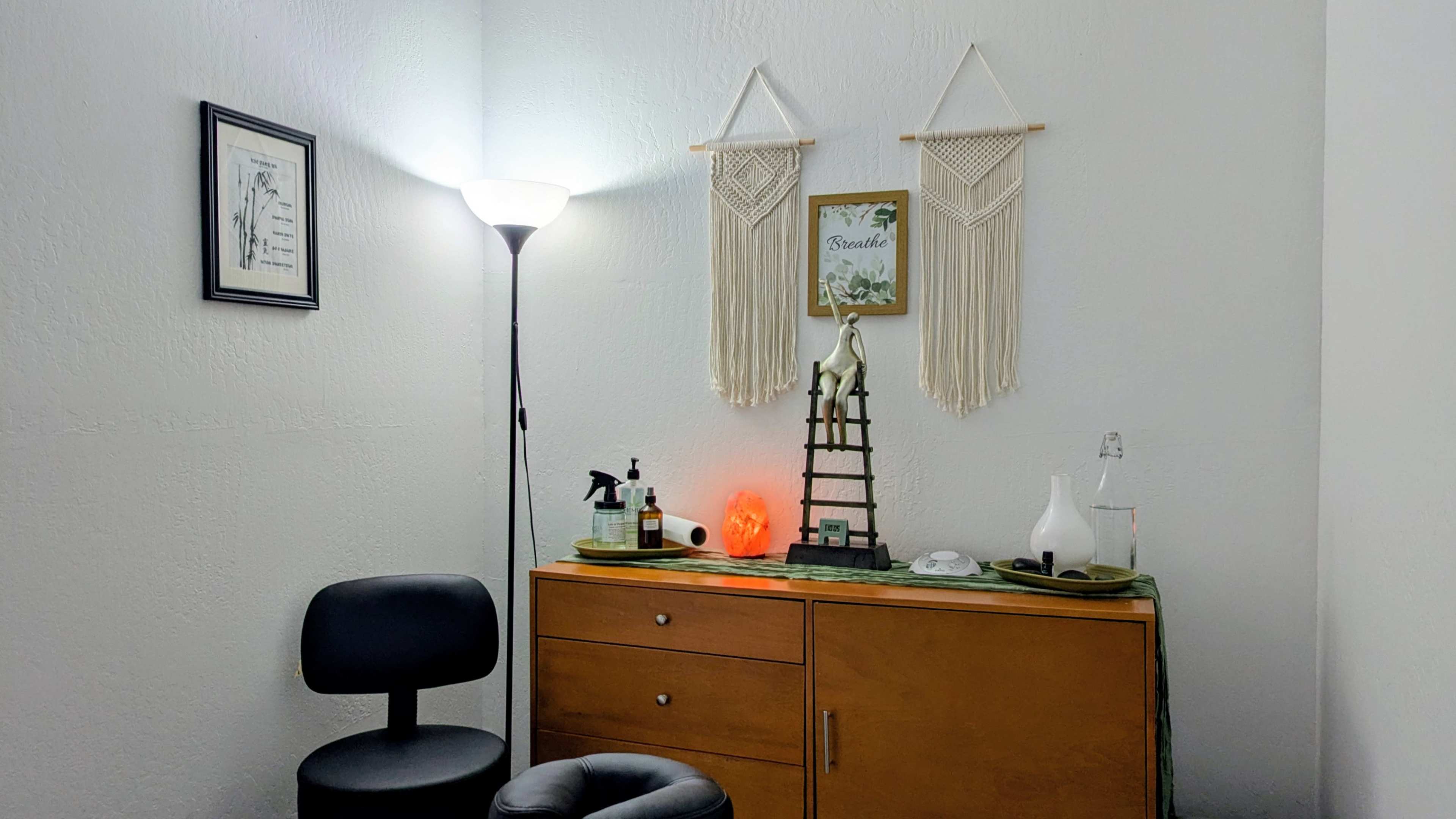 The image shows a small, well-decorated room featuring a wooden cabinet, a lamp, decorative wall hangings, and various items on a countertop.