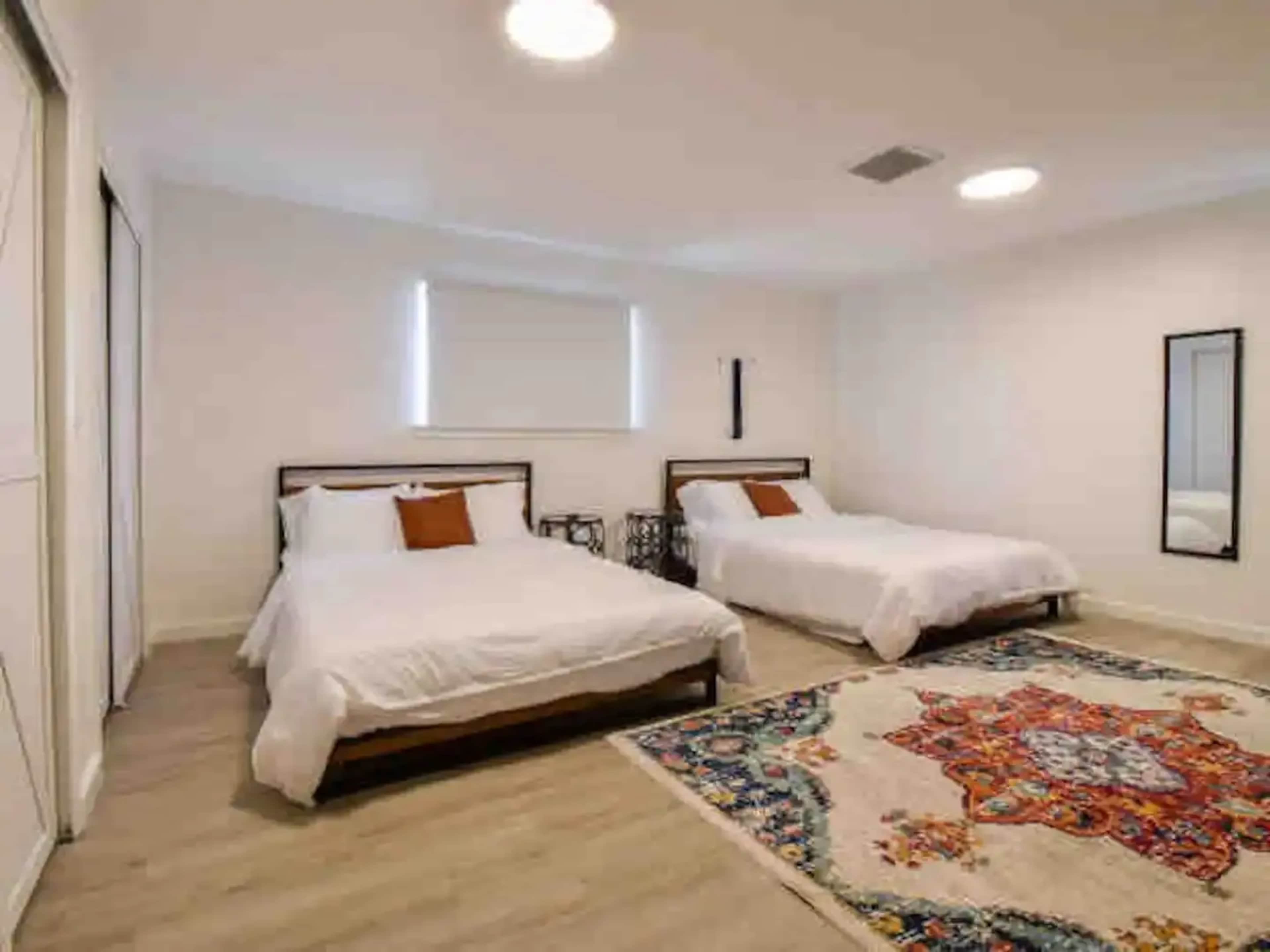 A spacious bedroom with two twin beds, a patterned rug on the floor, and a large mirror on the wall.