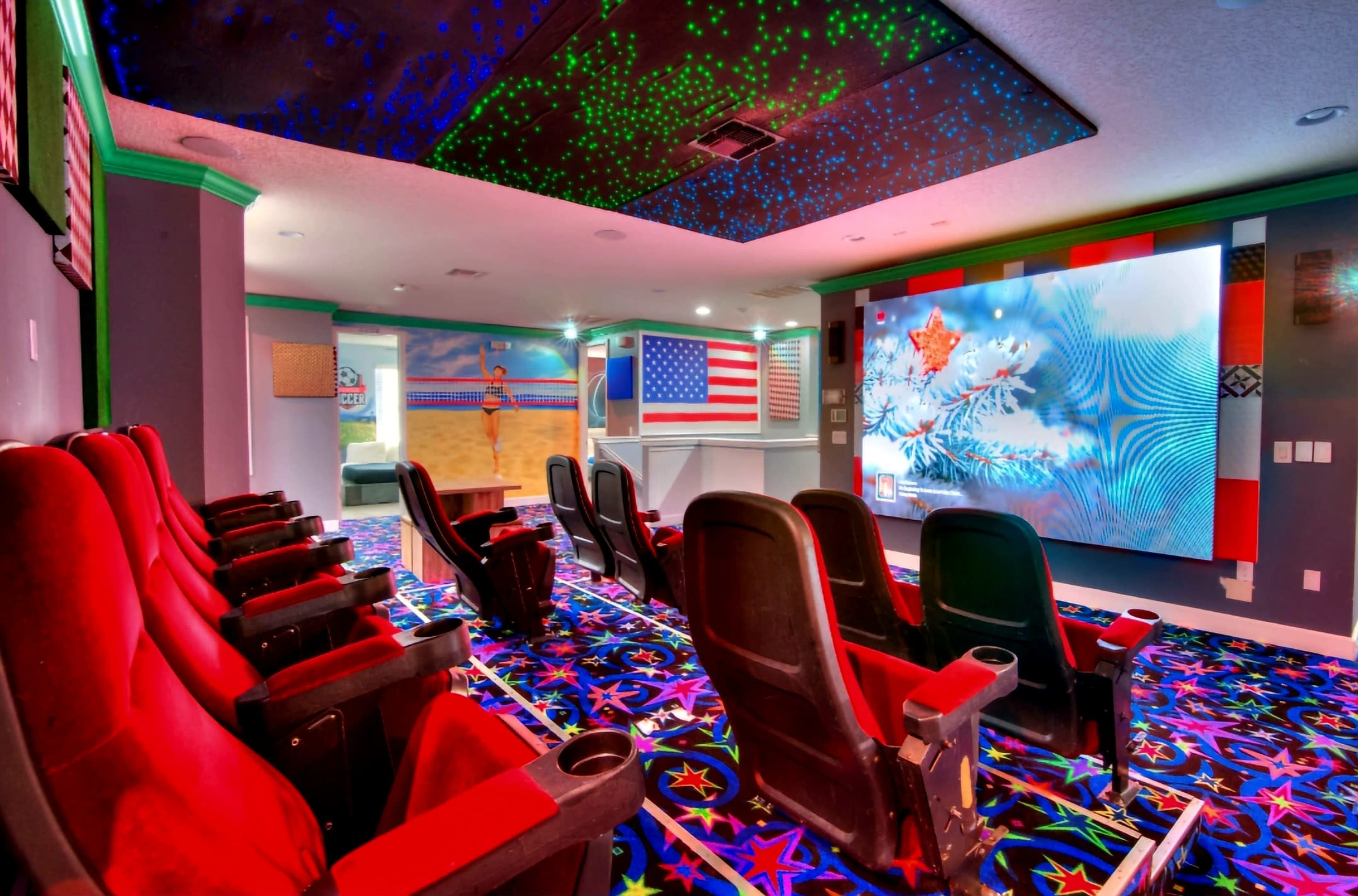 A home theater with red reclining chairs, a large projection screen displaying a winter scene, and colorful star-patterned carpet.