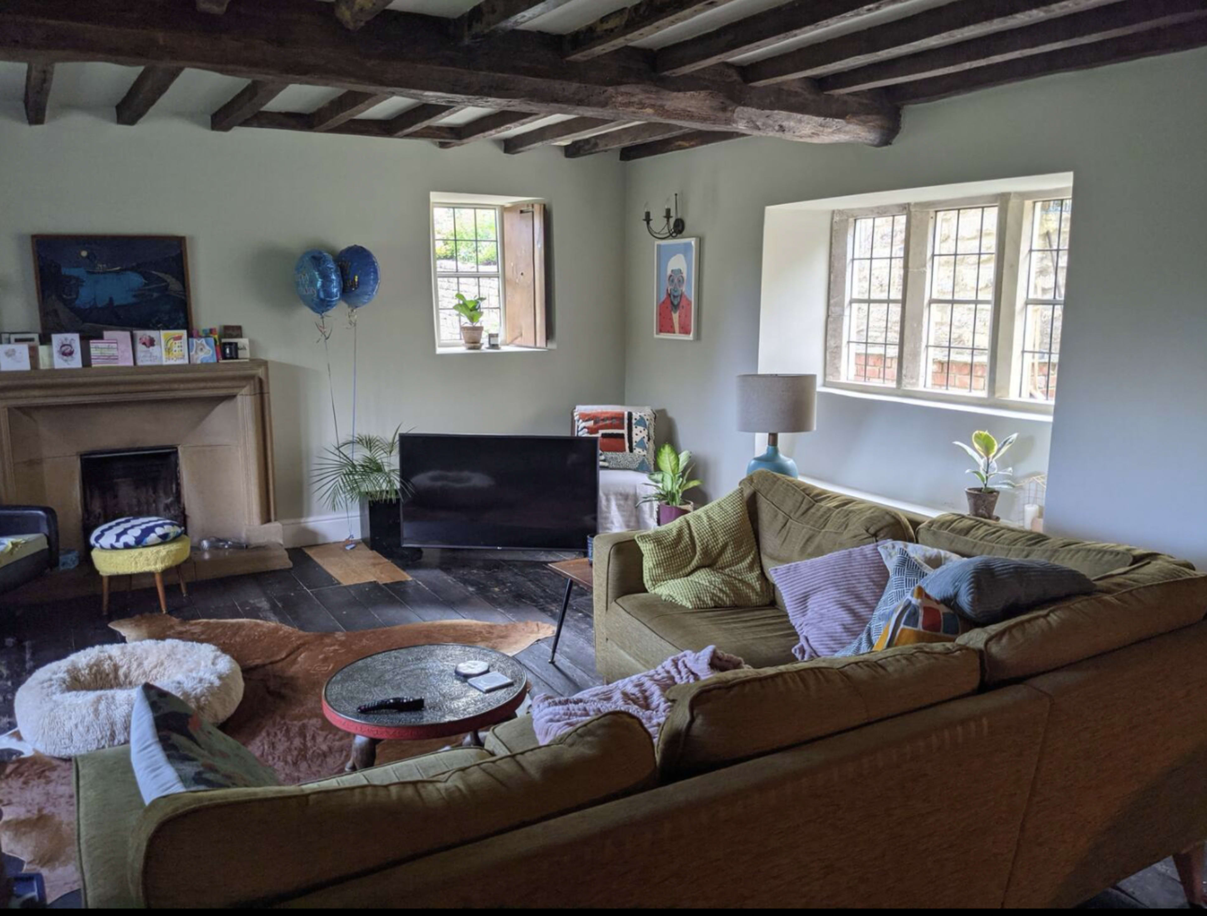 The living room features a green sectional sofa, a circular coffee table, and a television, with large windows allowing natural light to enter.