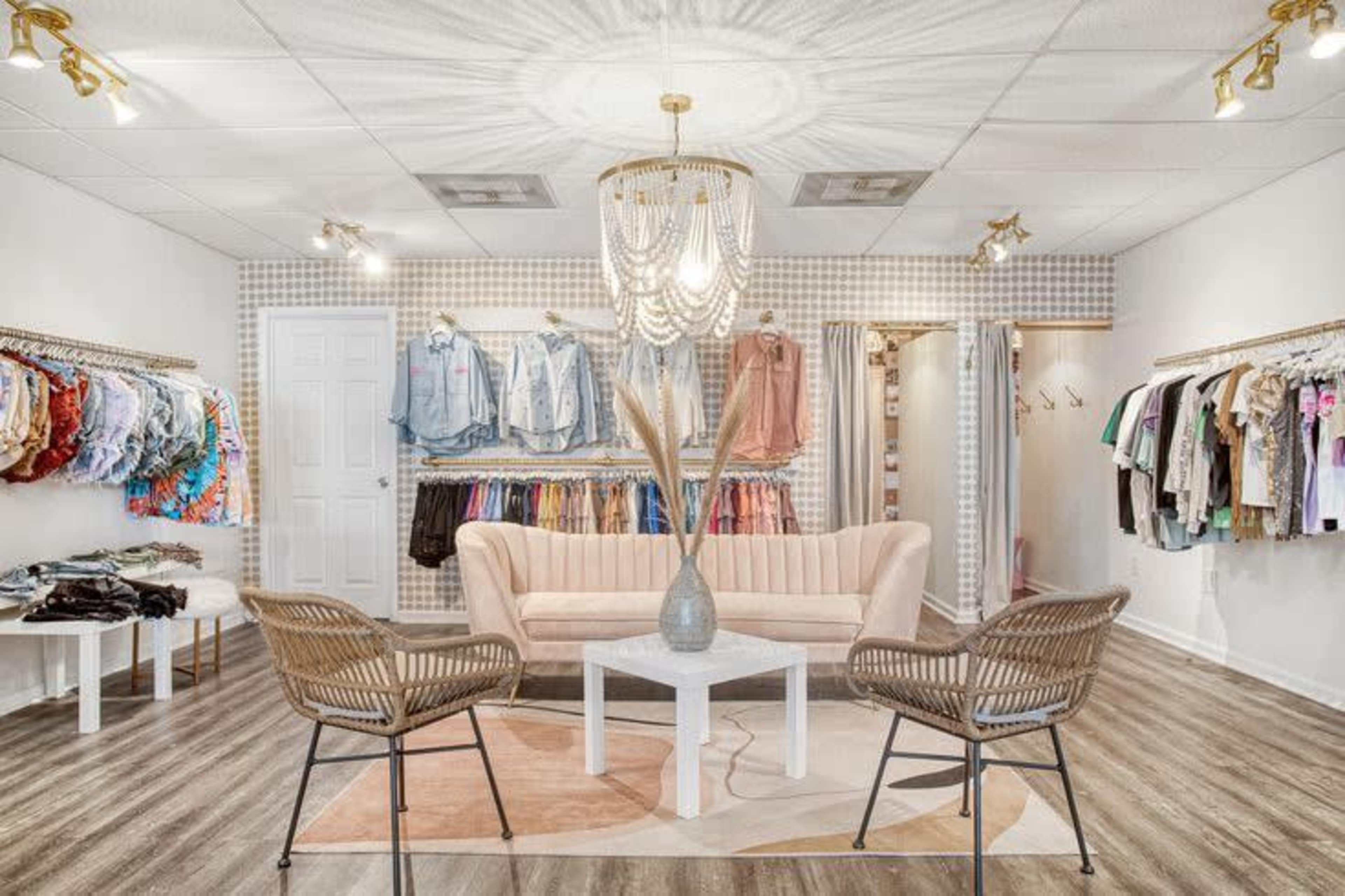 The image shows a clothing store interior featuring a pastel-colored sofa, a coffee table, and displays of various garments on racks along the walls.