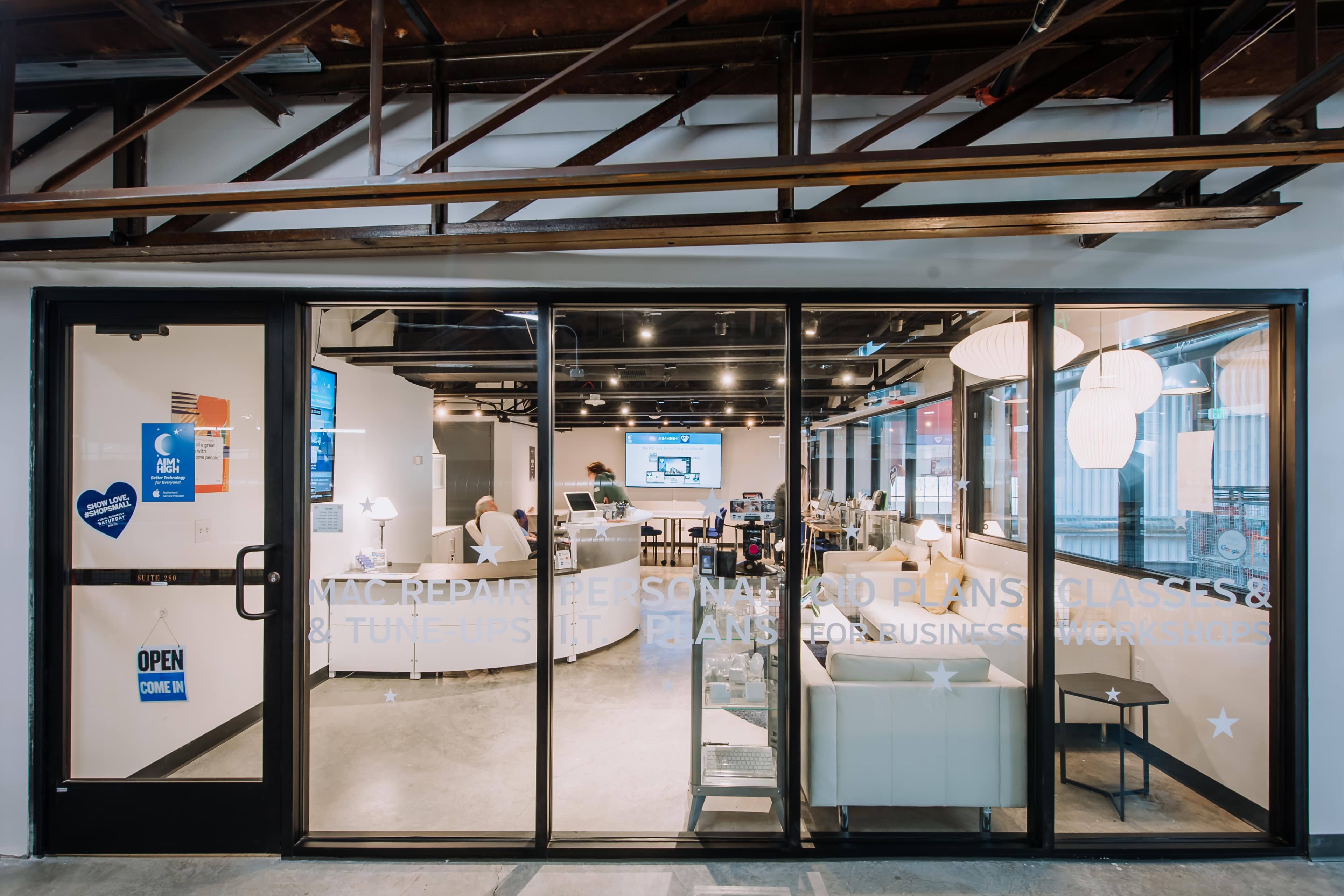 A glass entryway displays a modern office space with seating areas and digital screens visible inside.