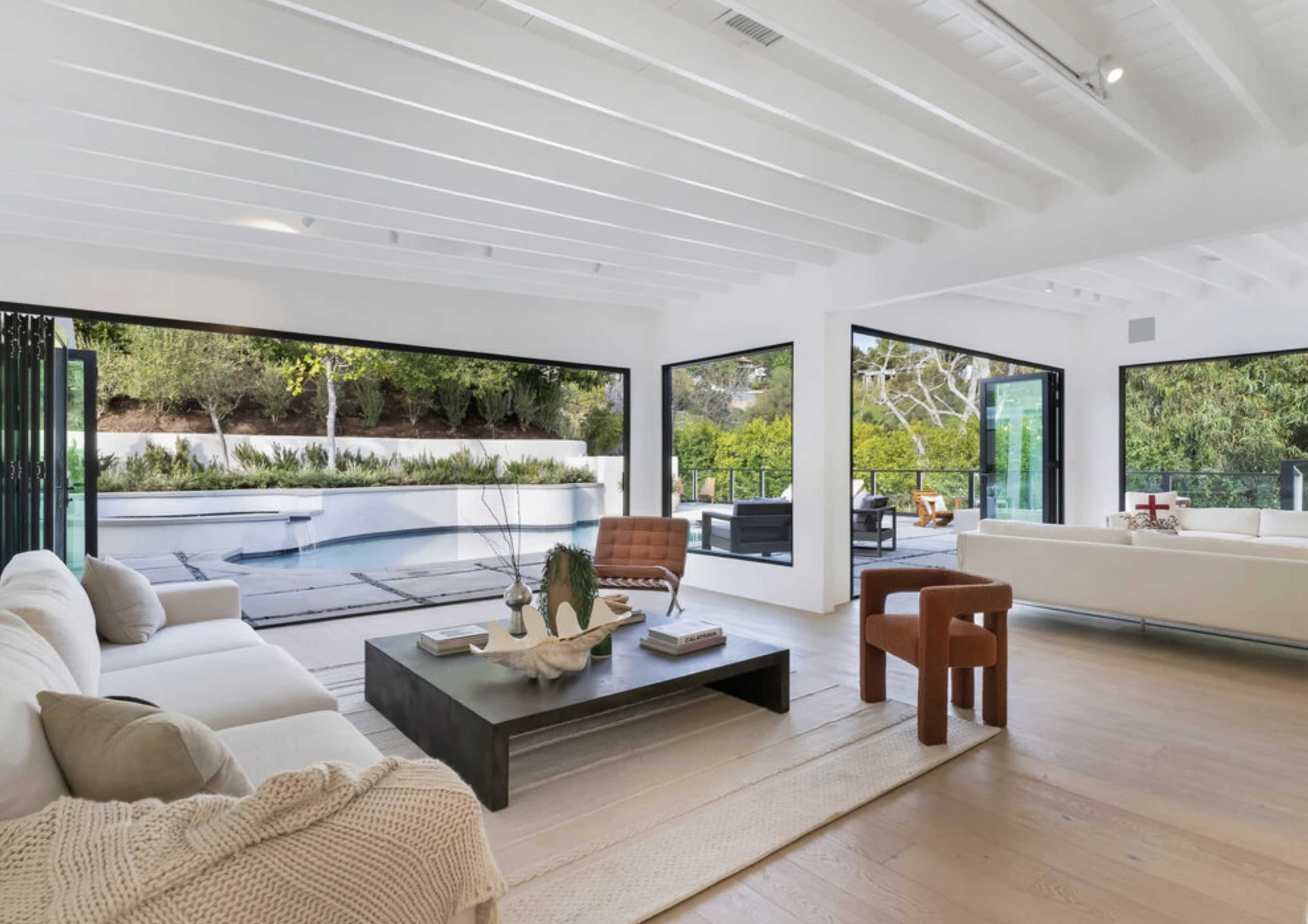 A modern, open-concept living room with large windows that overlook a swimming pool and landscaped yard.