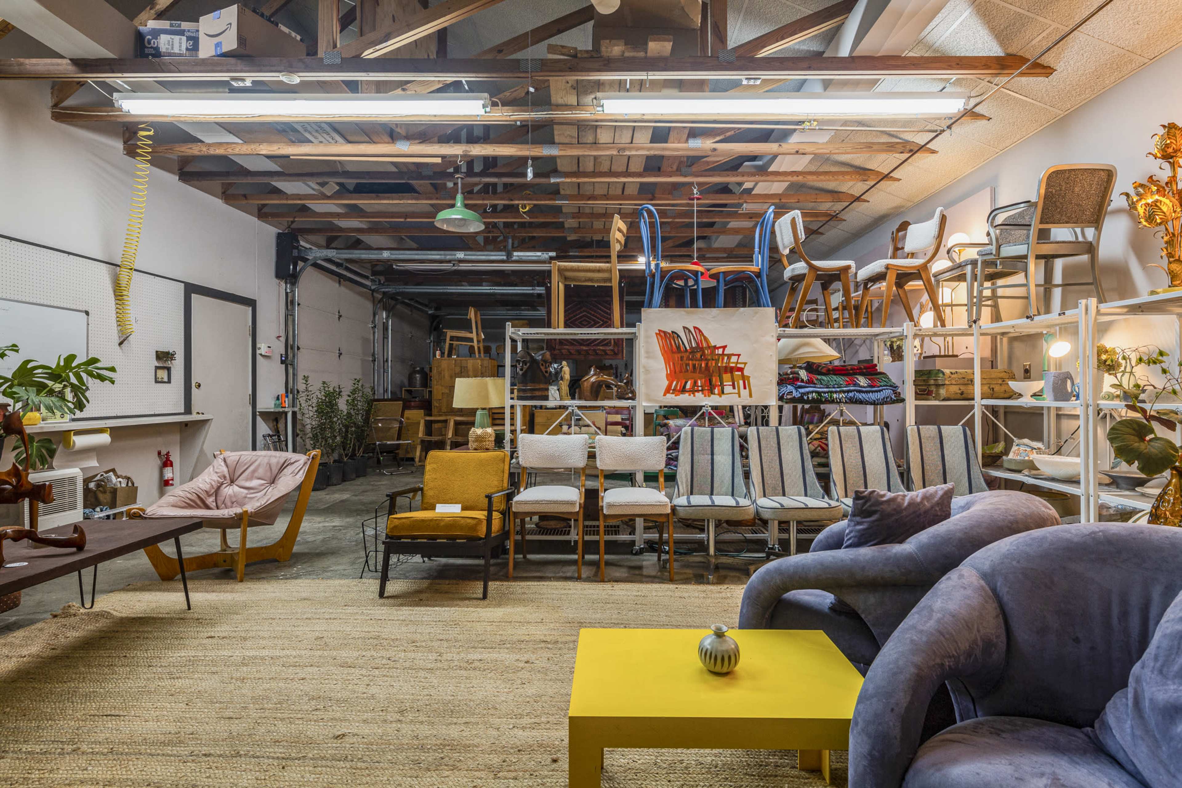 A spacious warehouse displays an assortment of furniture, including chairs and couches, along with decorative items on shelving units.