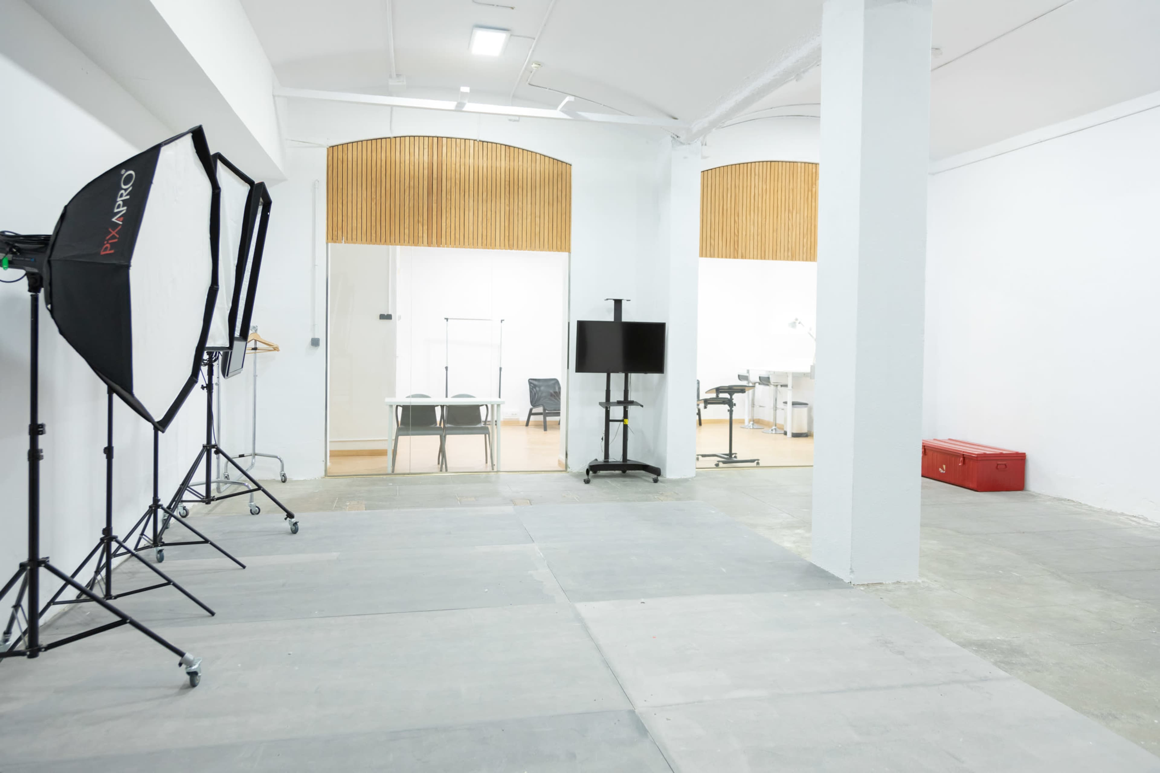 A spacious, empty studio with photography equipment on the left and an office area with wooden panels in the background.
