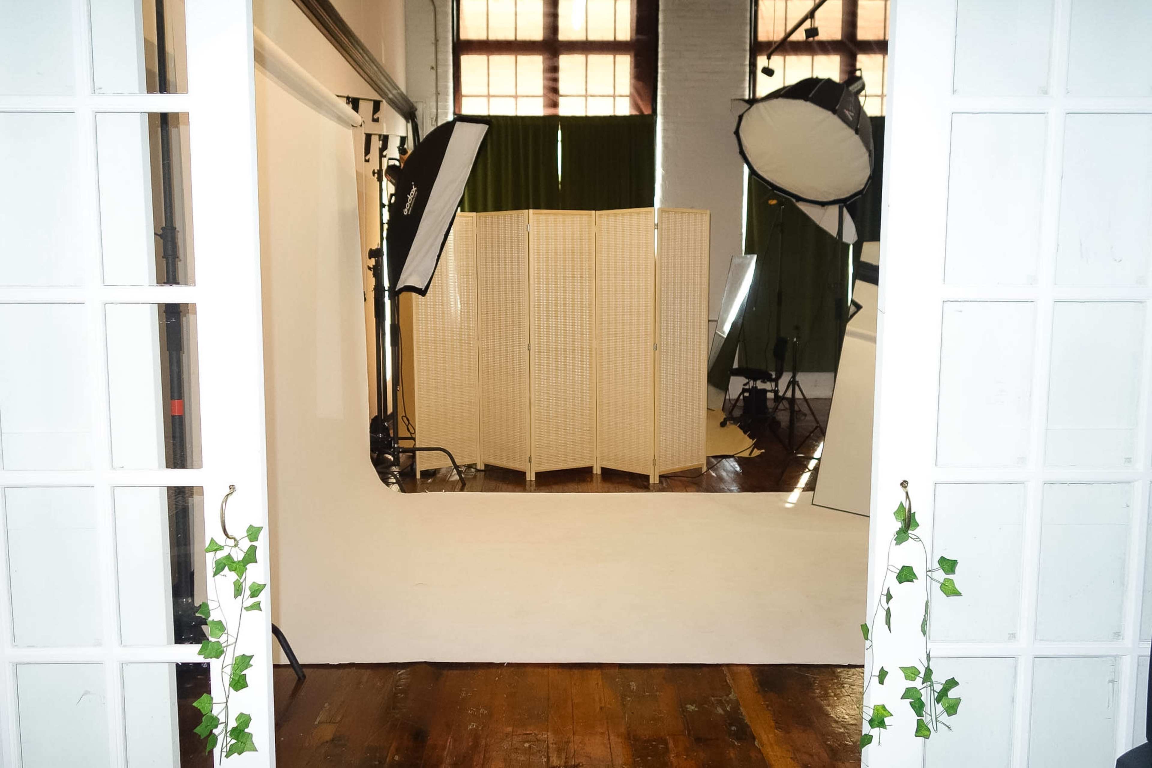 The image shows a photo studio with a large backdrop, lighting equipment, and a folding screen in the center.