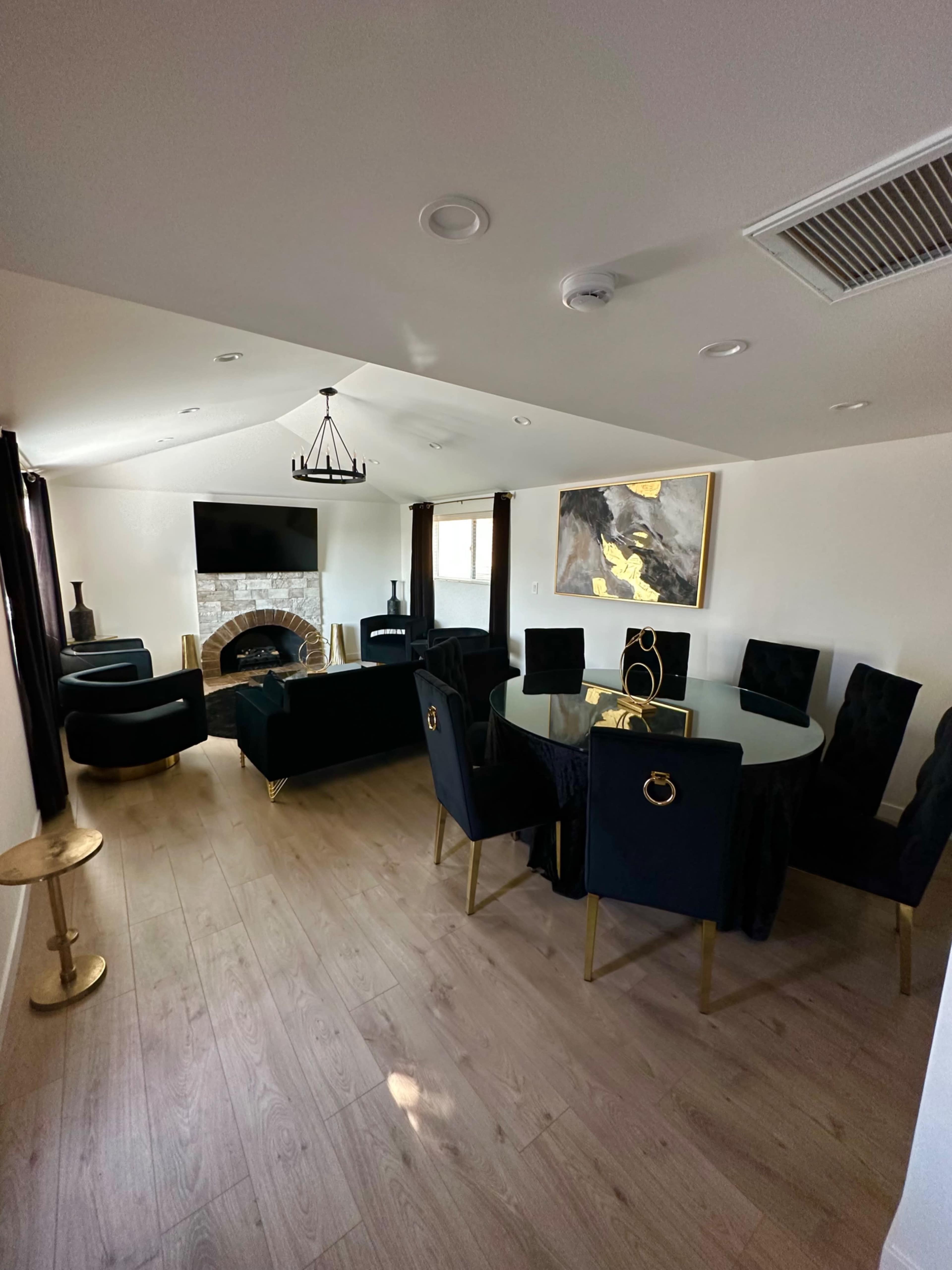 A modern living room features a black seating area, a circular dining table, a fireplace, and an artwork on the wall.