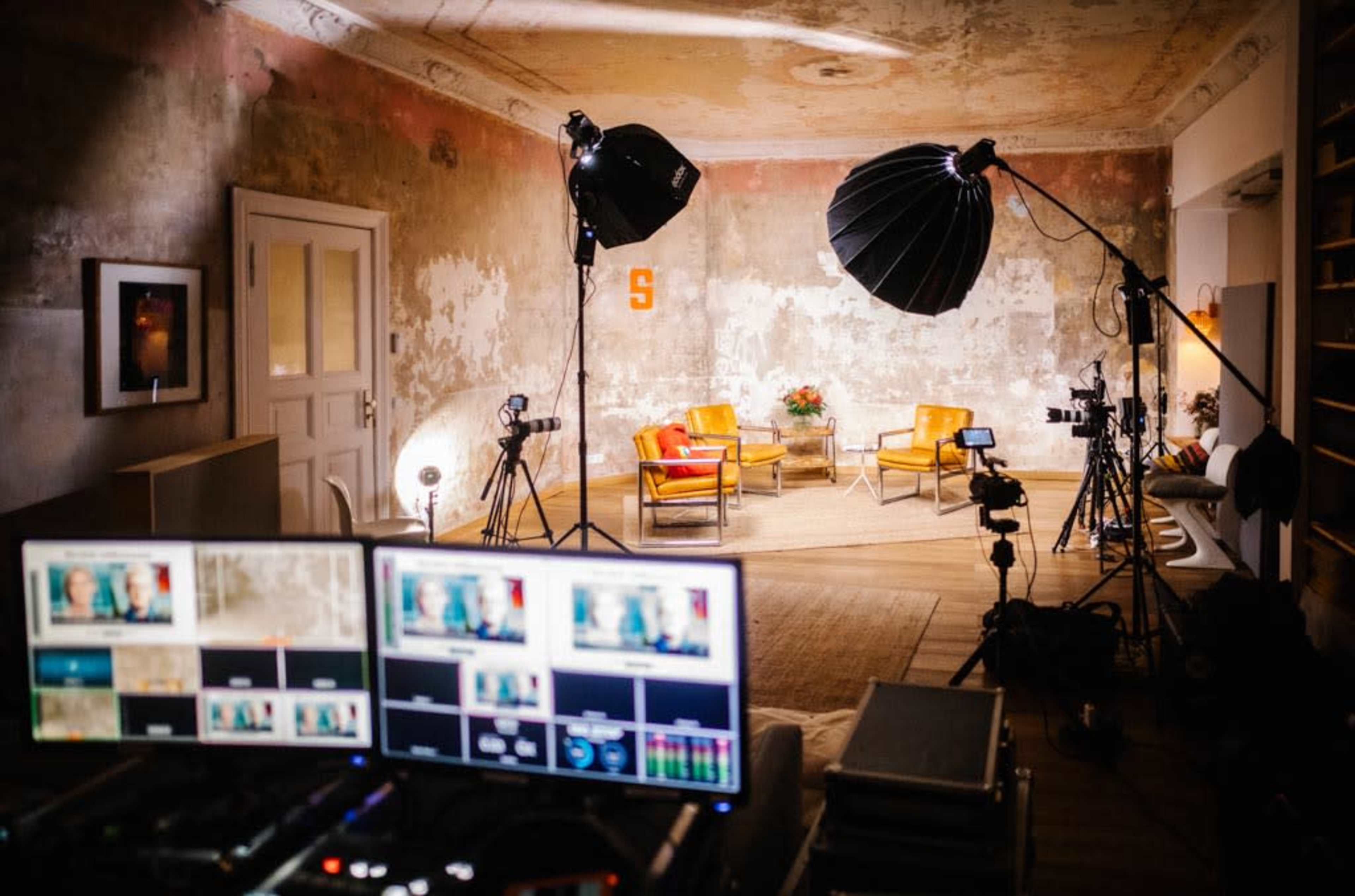 The image shows a well-equipped video production studio featuring two yellow chairs and various lighting and camera equipment in a rustic room.