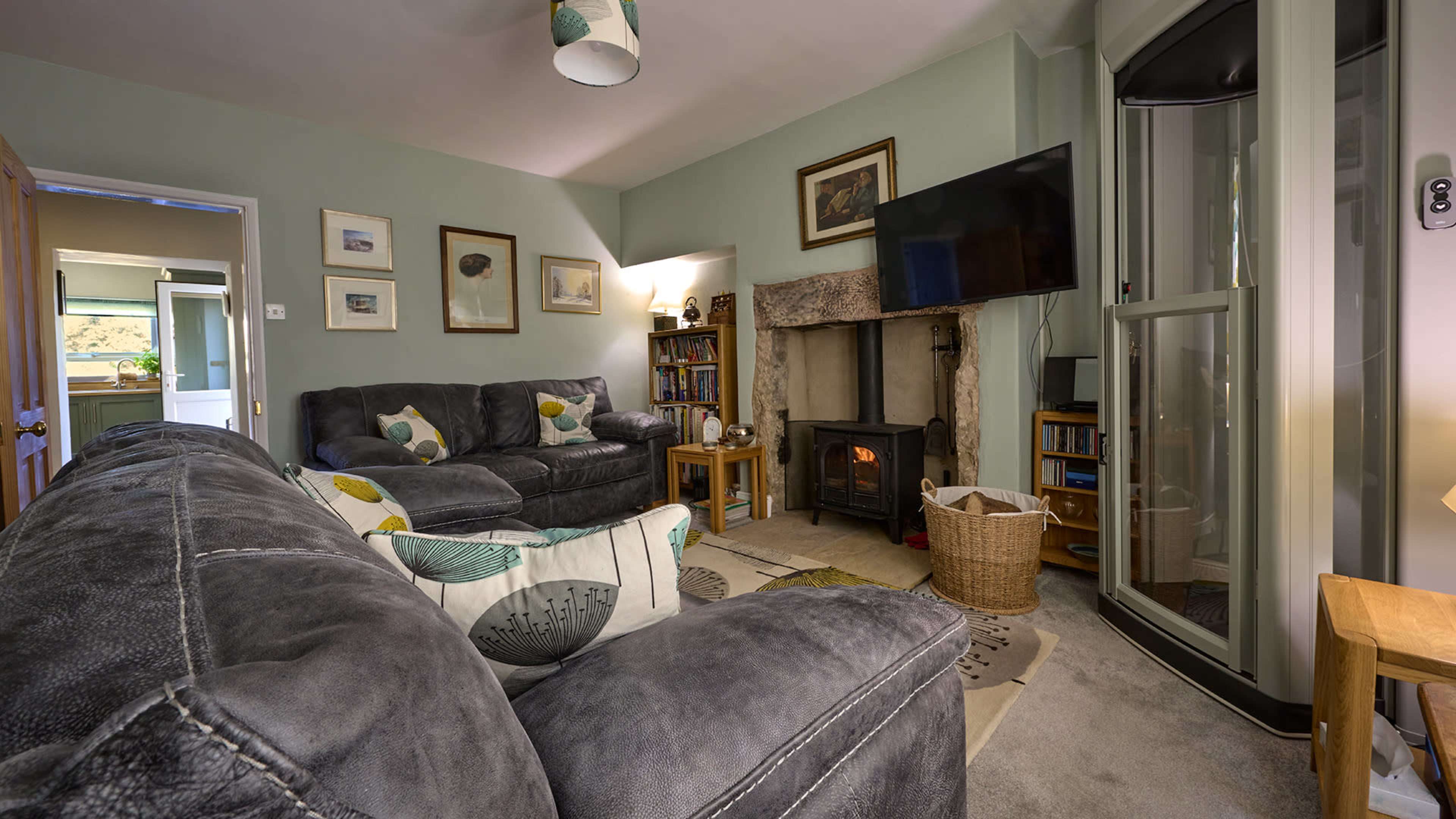 The image shows a cozy living room featuring a fireplace, two couches, a wooden table, and a glass-enclosed shower in the corner.