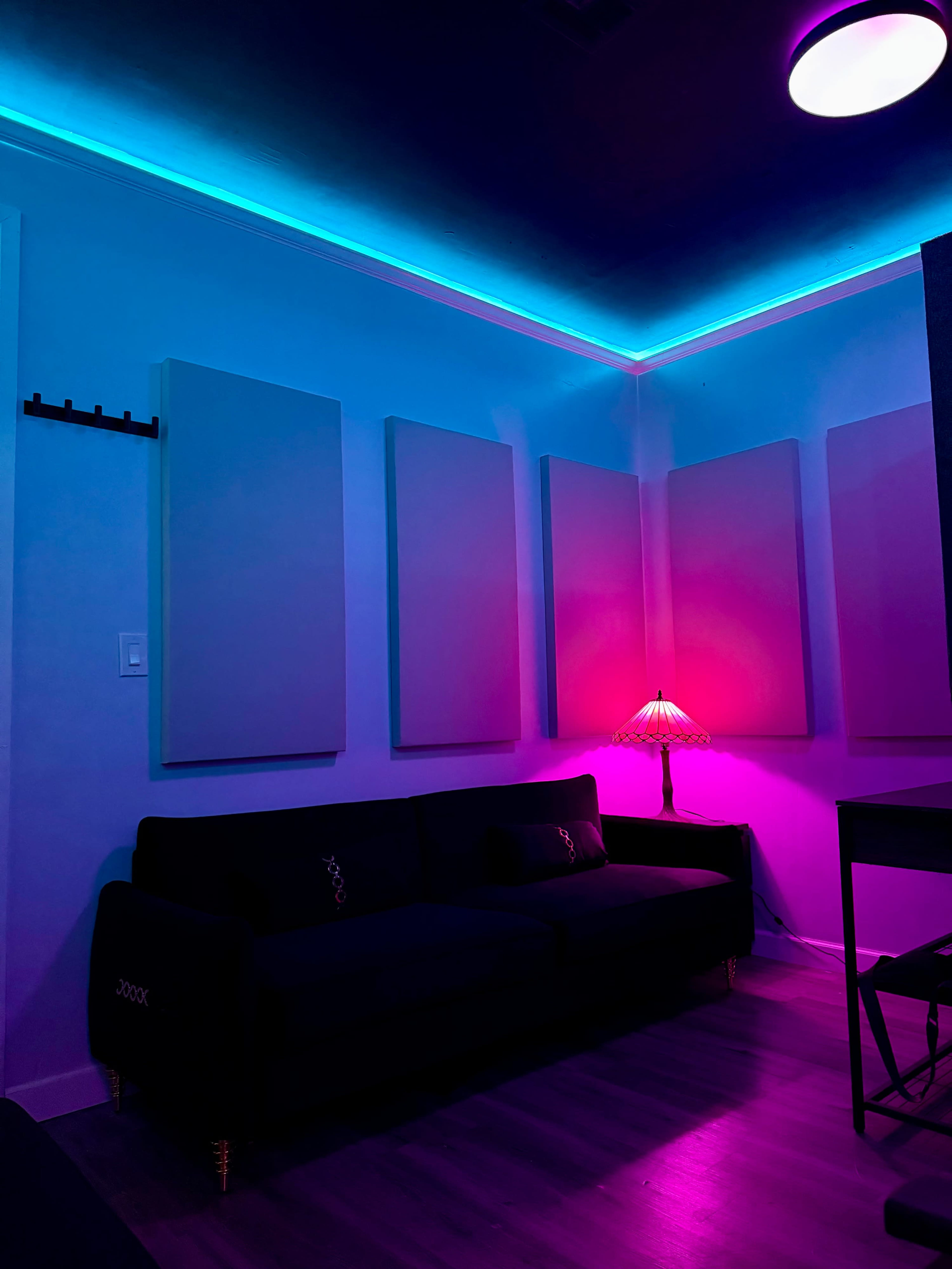 The image shows a dimly lit room with acoustic panels on the walls, a black sofa, and a lamp casting pink light.