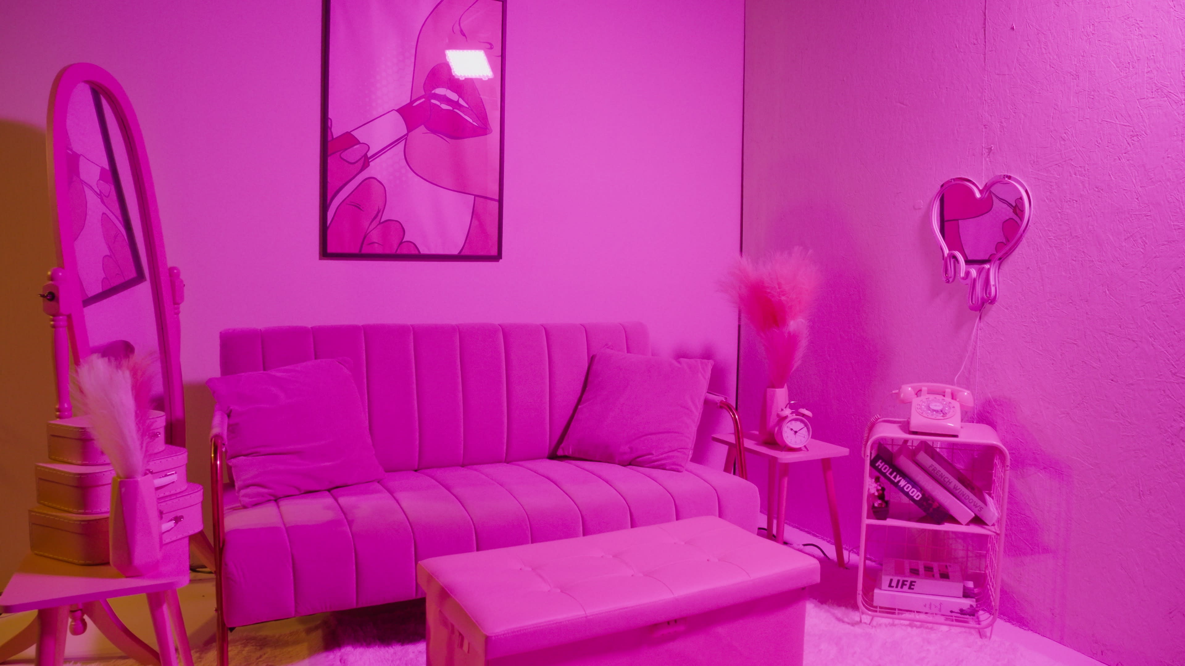 The room features a pink-themed sitting area with a velvet sofa, a small coffee table, a vintage telephone, and a mirror against the wall, all illuminated by pink lighting.