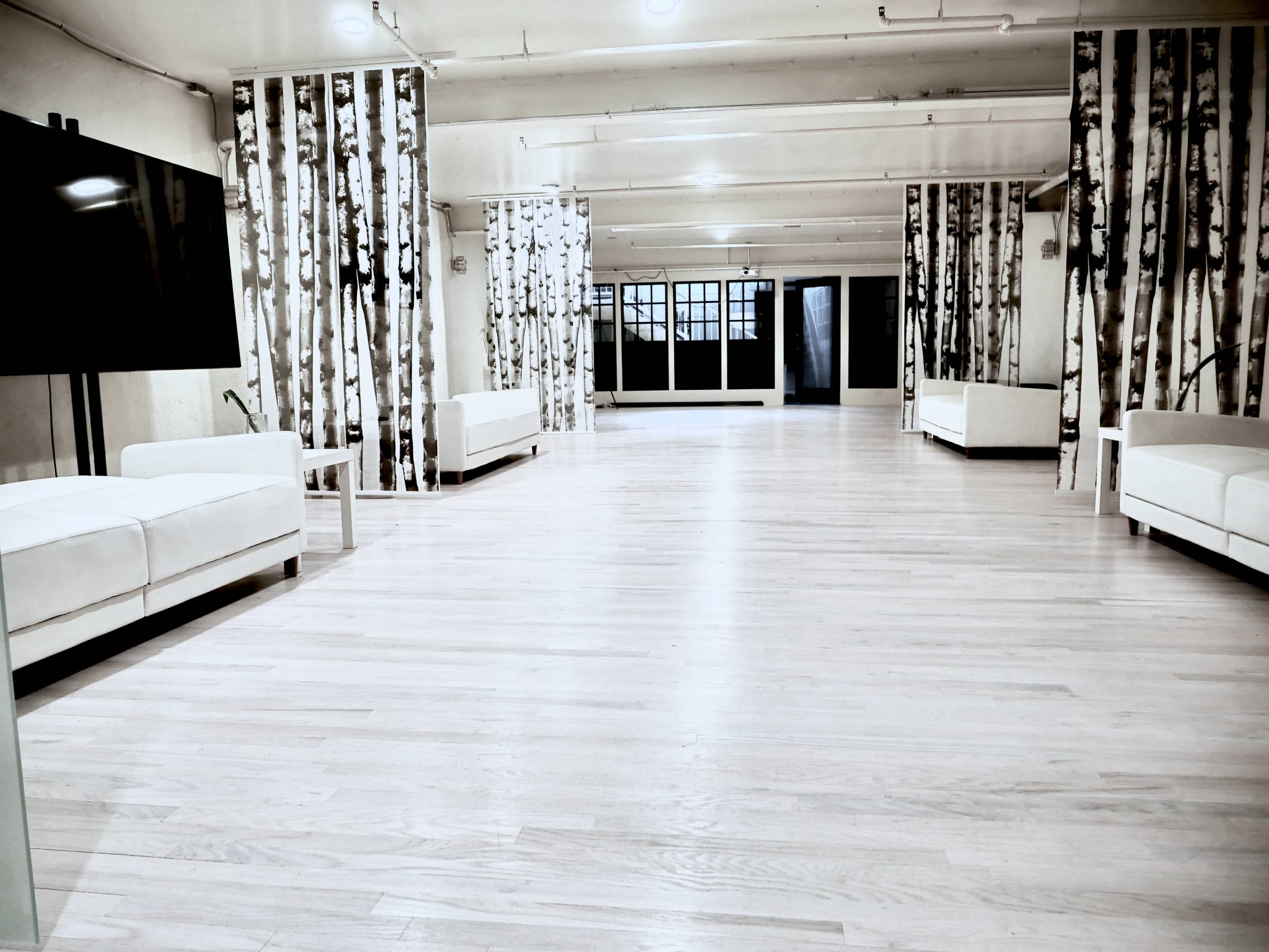 An empty, minimalist interior space with light wooden flooring, white sofas, and walls featuring a tree-pattern wallpaper.