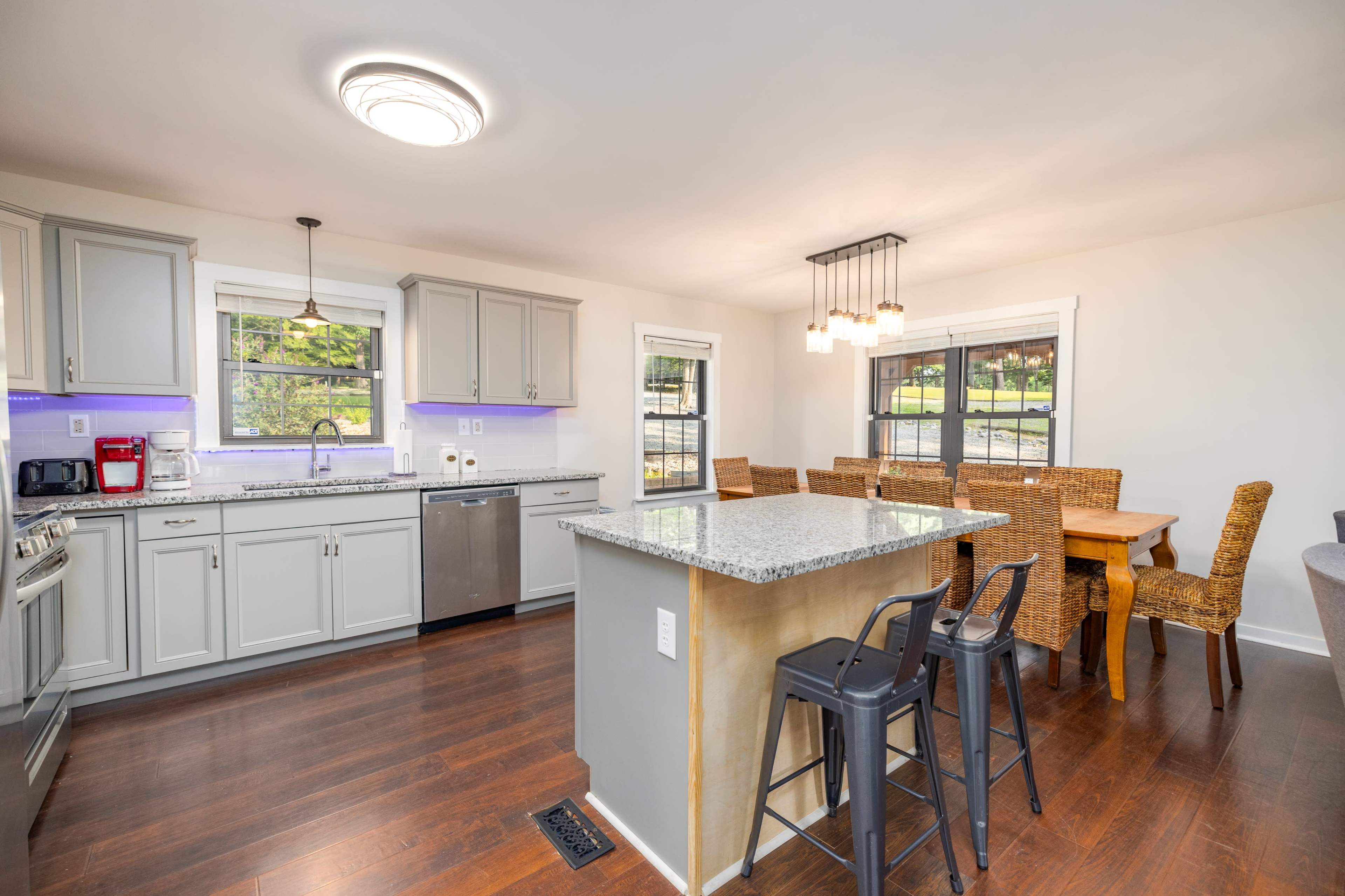 A modern kitchen features gray cabinets, a granite island, and a dining area with woven chairs and a wooden table.