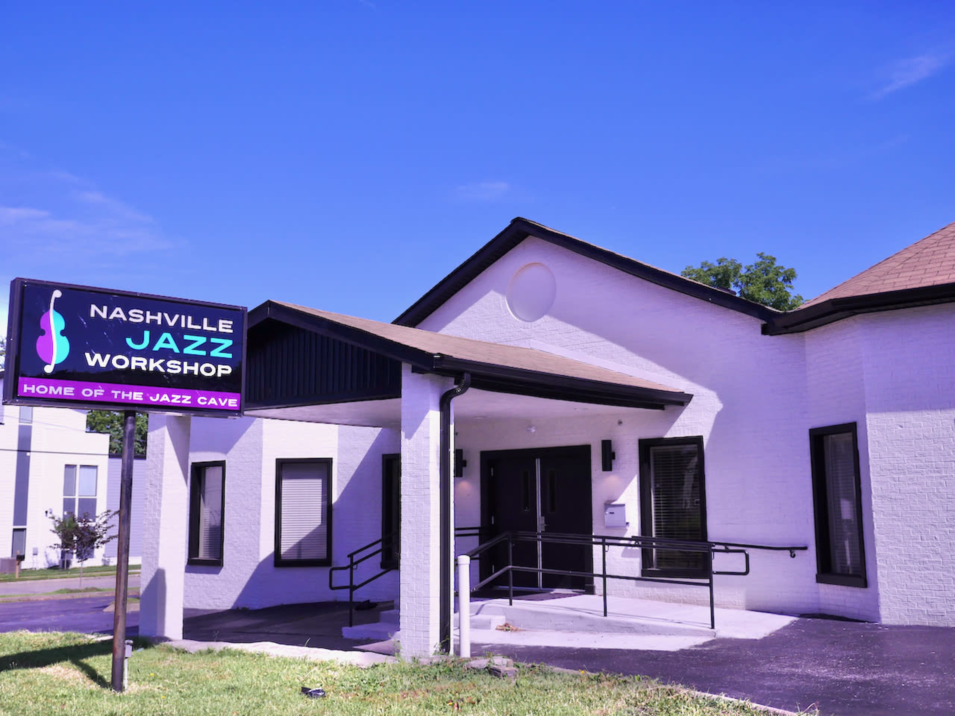 The image shows a white building with a sloped roof and a sign that reads "NASHVILLE JAZZ WORKSHOP" next to an entrance ramp.