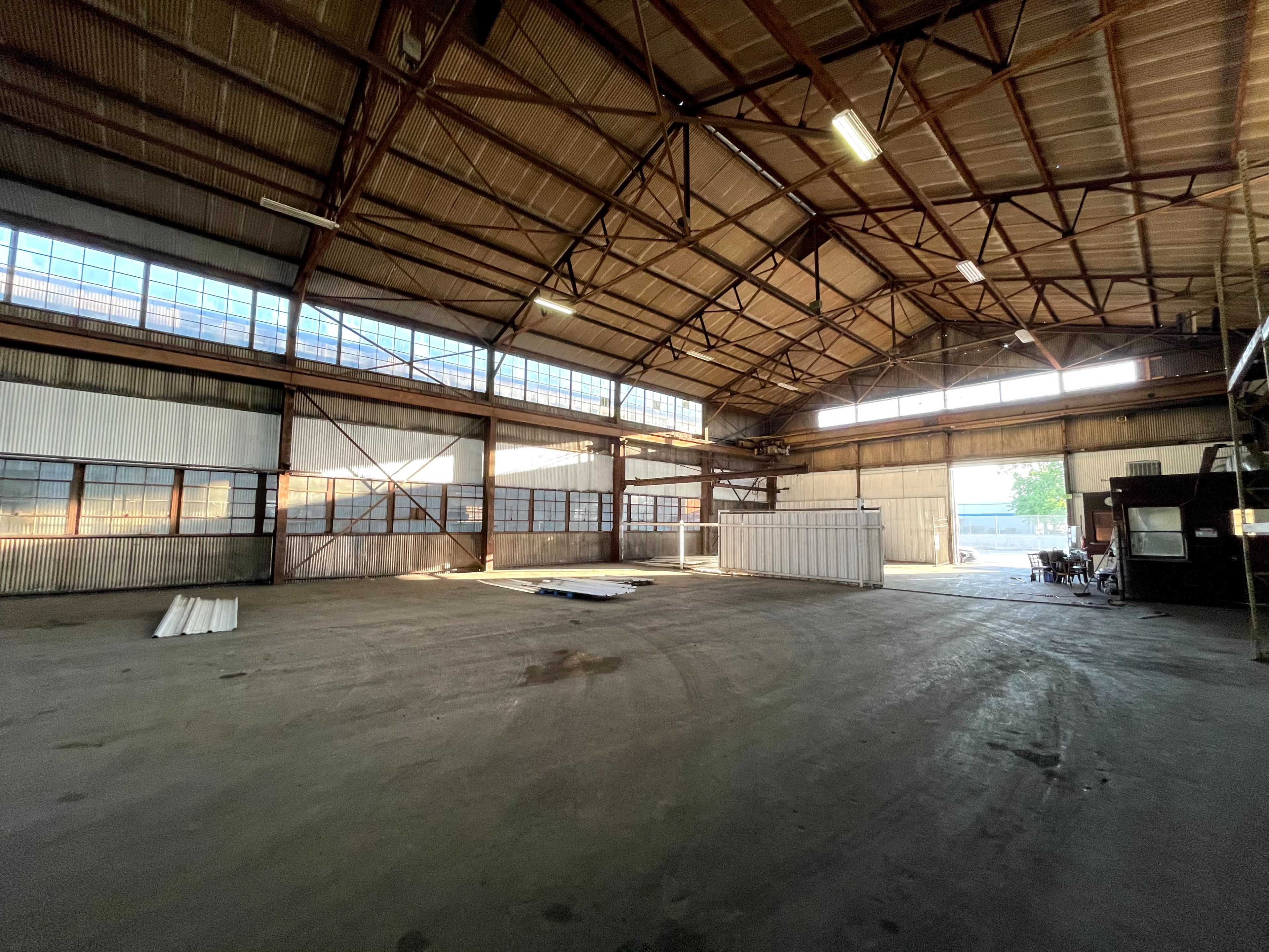 A large, empty industrial warehouse with high ceilings and large windows allowing natural light to enter.