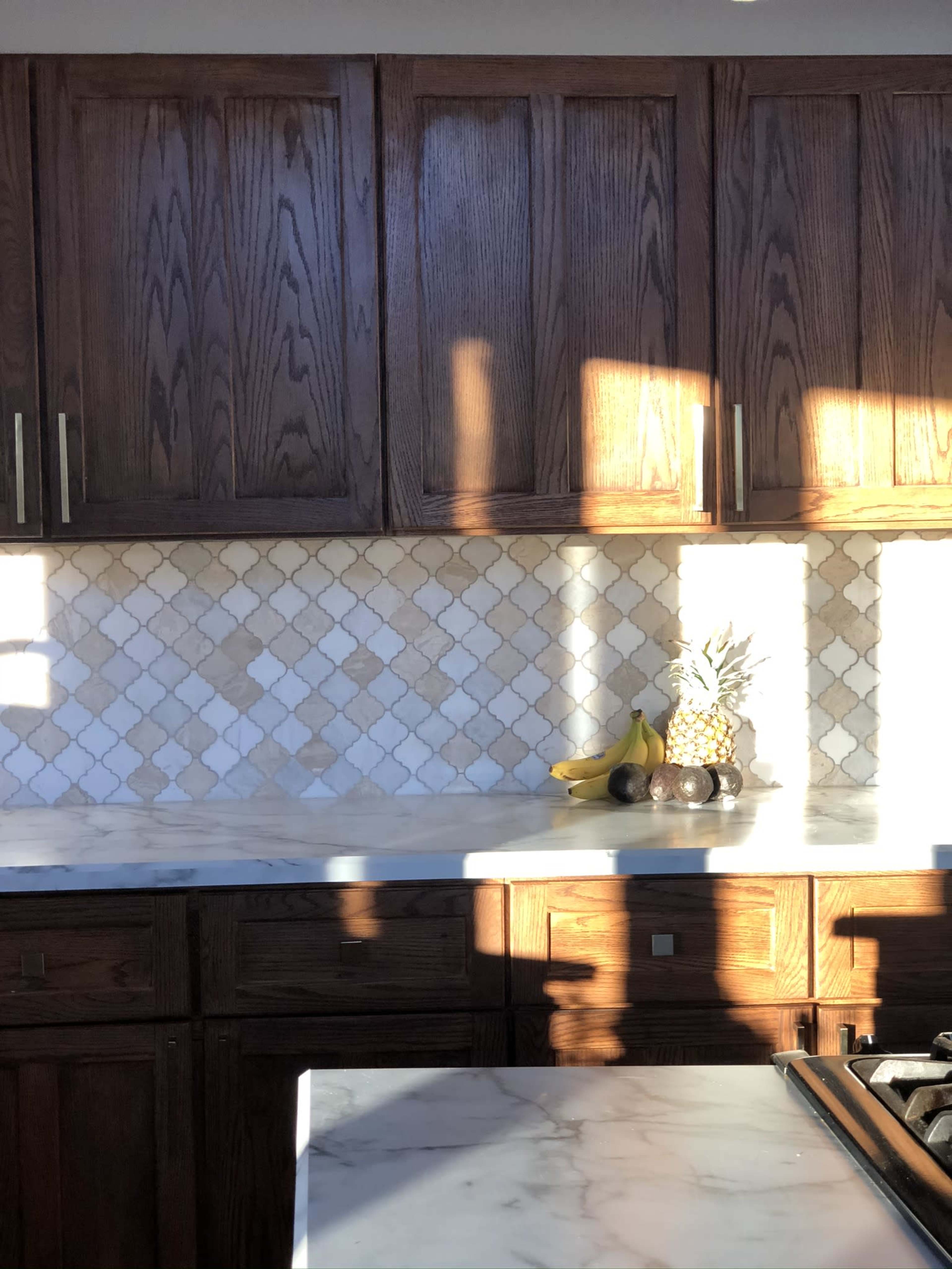 The kitchen features dark wooden cabinets, a marble countertop, and a backsplash of diamond-patterned tiles with fruits displayed on the counter.