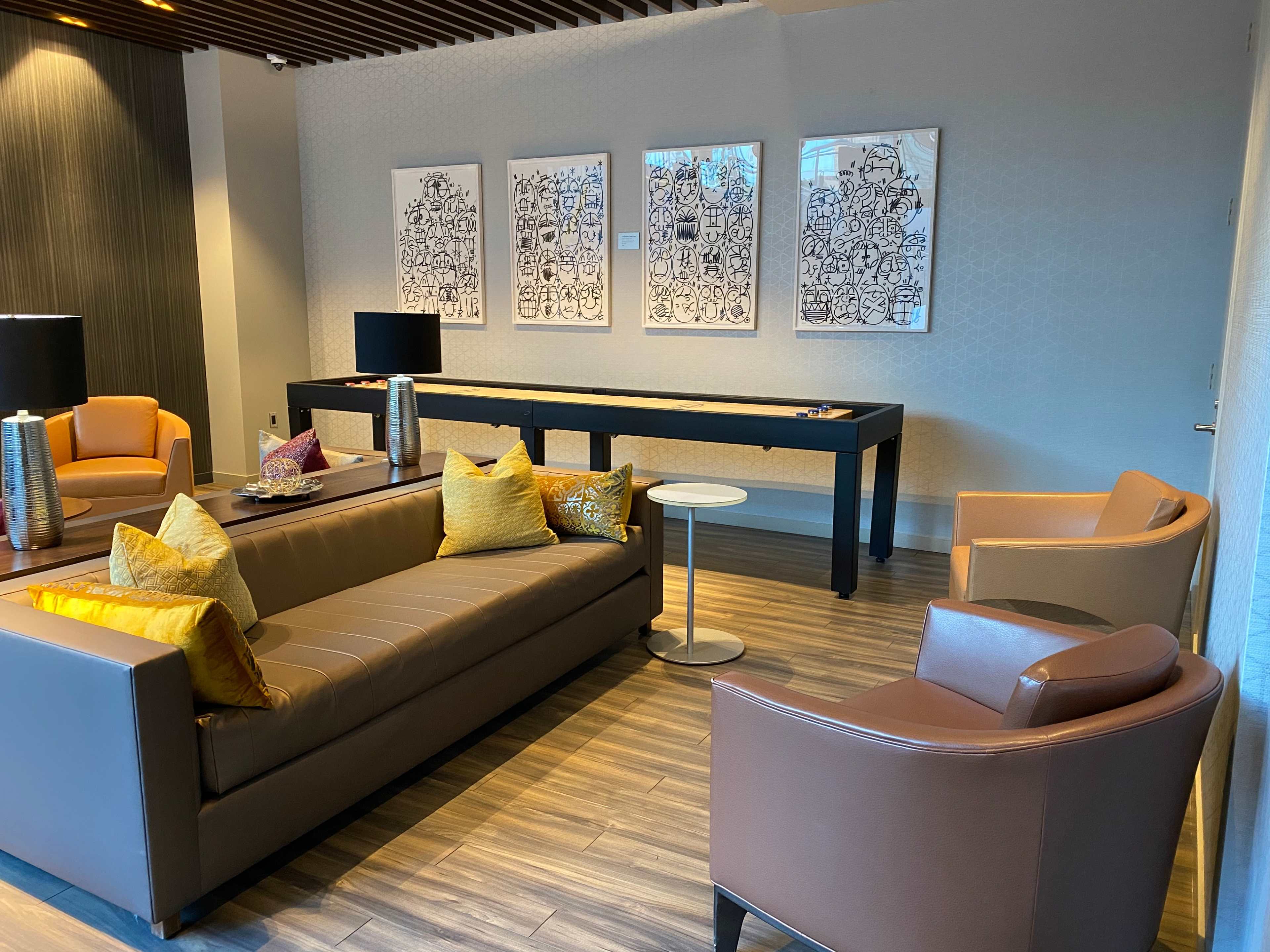 A modern lounge area features a gray sofa, two armchairs, a small side table, and three framed artworks on the wall.