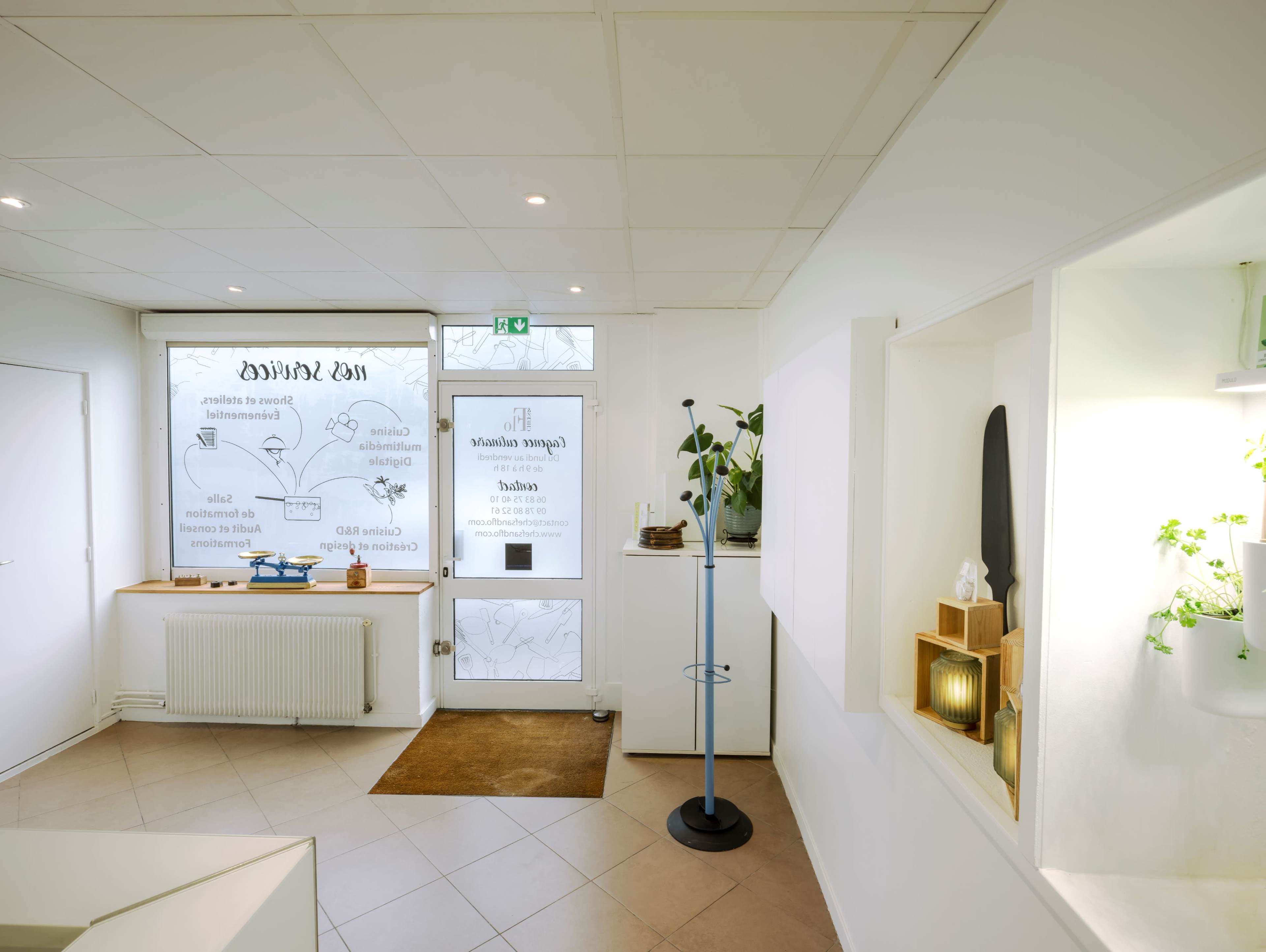 A bright interior of a modern space with a reception area, featuring a large window displaying text, plants, and a variety of decorative items on the walls.