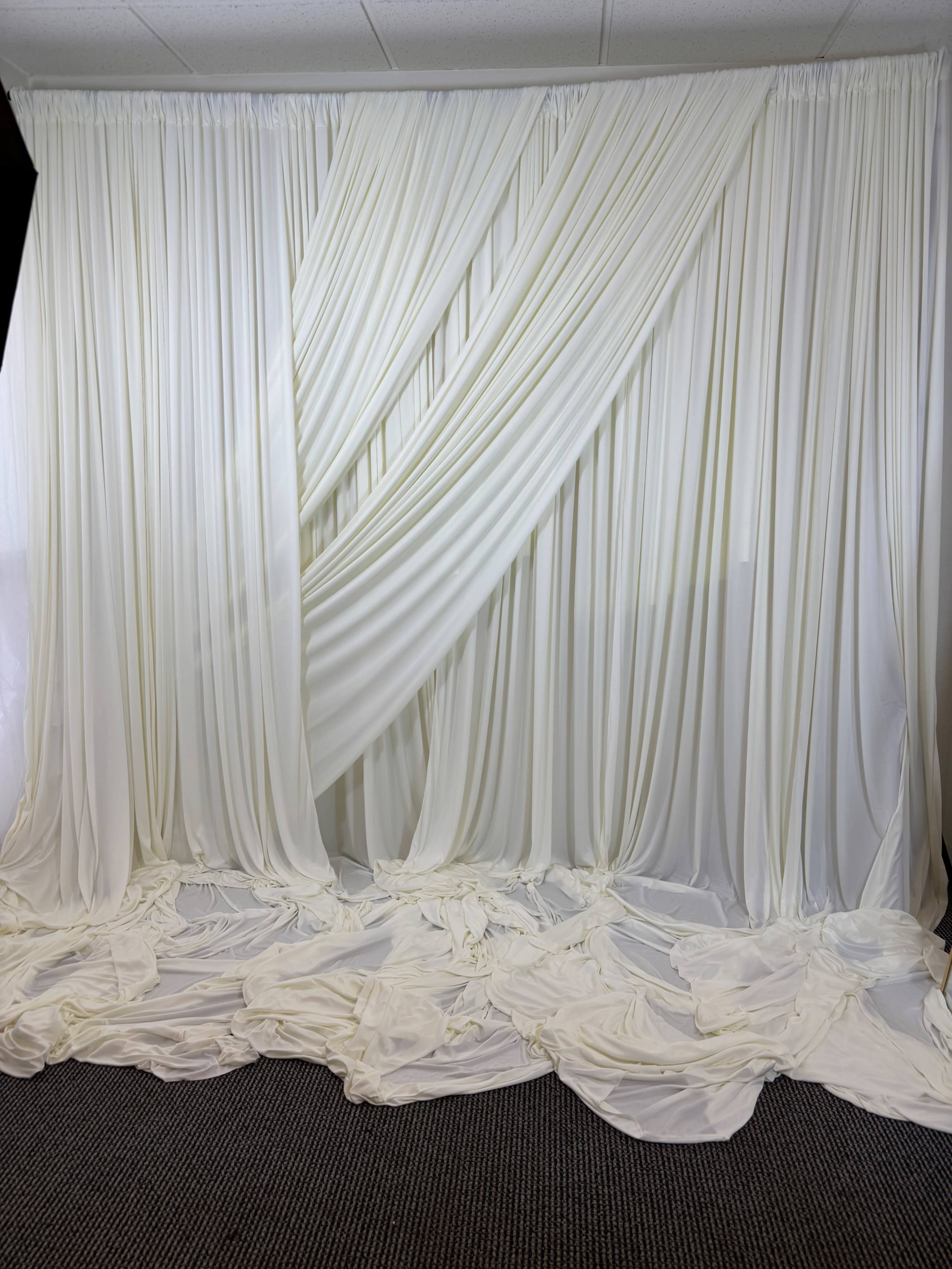 The image shows a backdrop of white draped fabric arranged with folds and cascades on the floor.