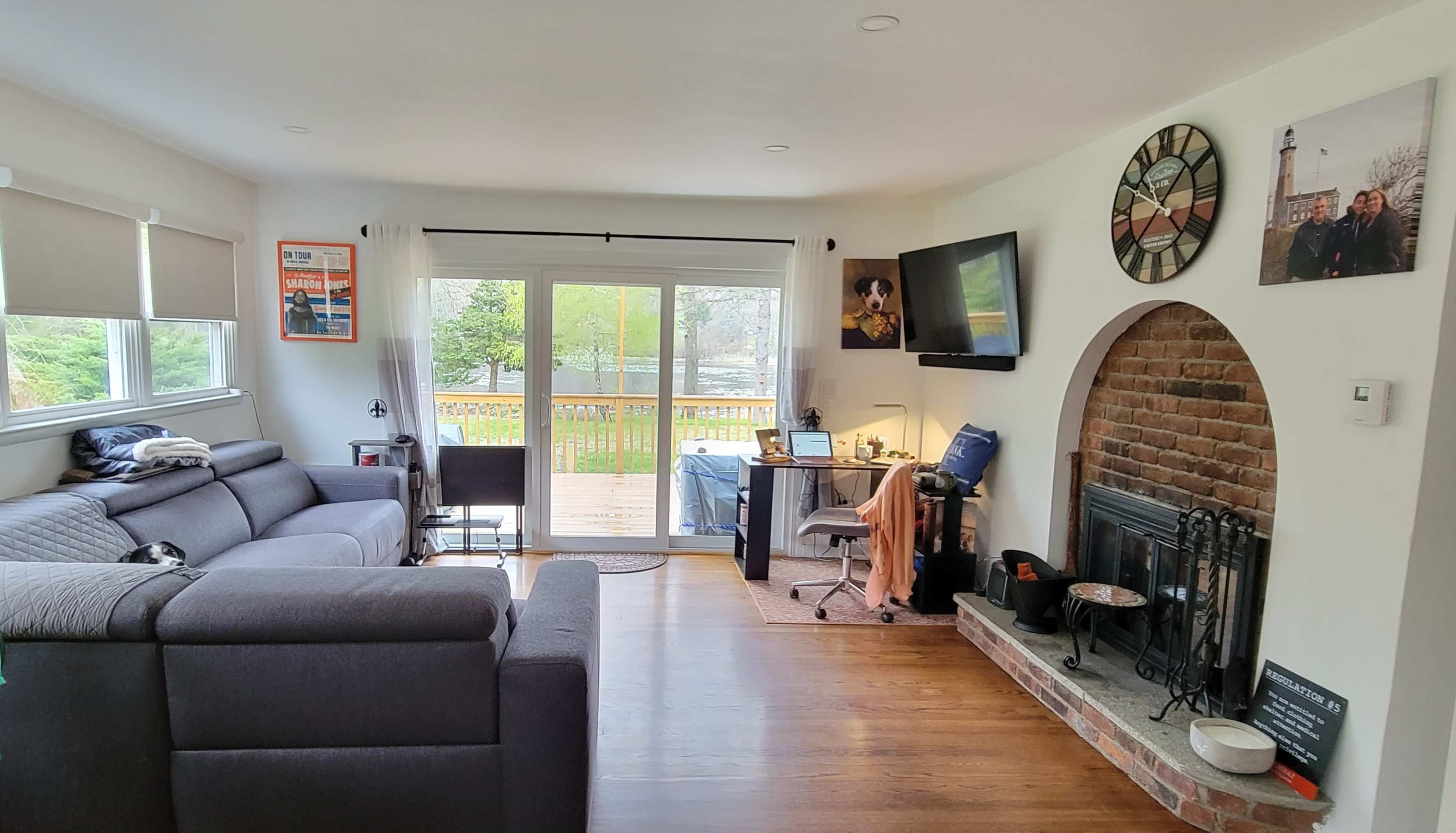 The living room features a gray sectional sofa, a brick fireplace, a desk with a computer, and large sliding glass doors leading to a deck.