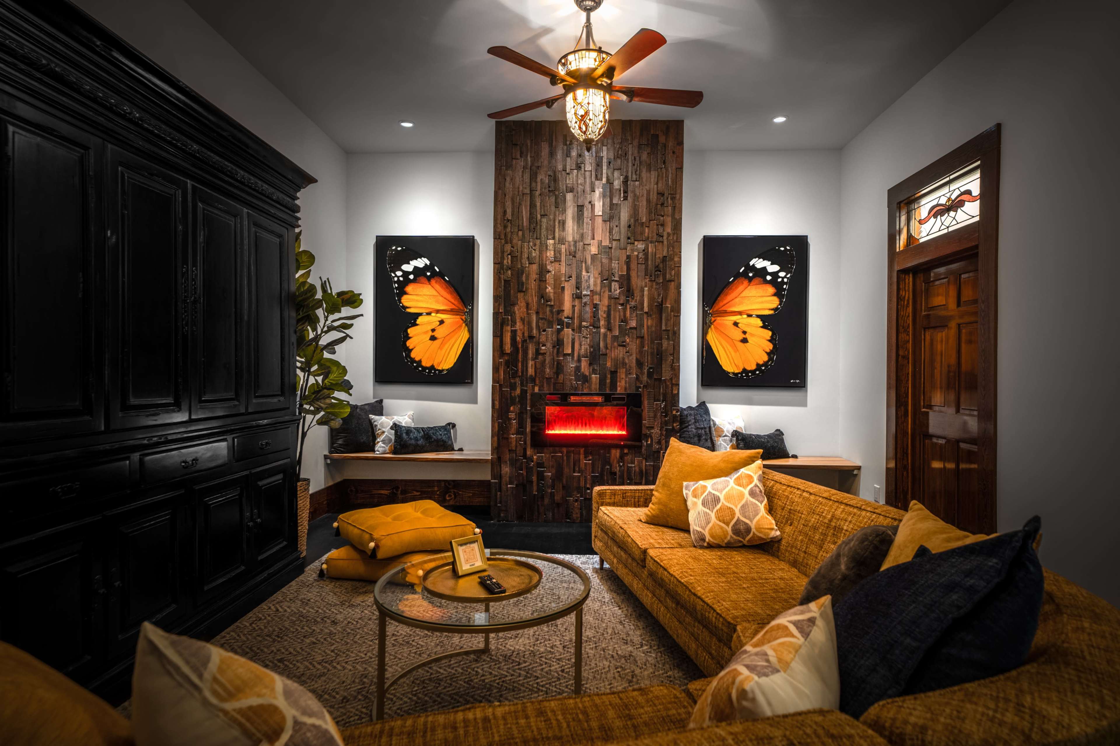 The living room features a cozy arrangement with a brown sectional sofa, a round coffee table, and large butterfly artwork on a wooden accent wall, complemented by a modern electric fireplace.