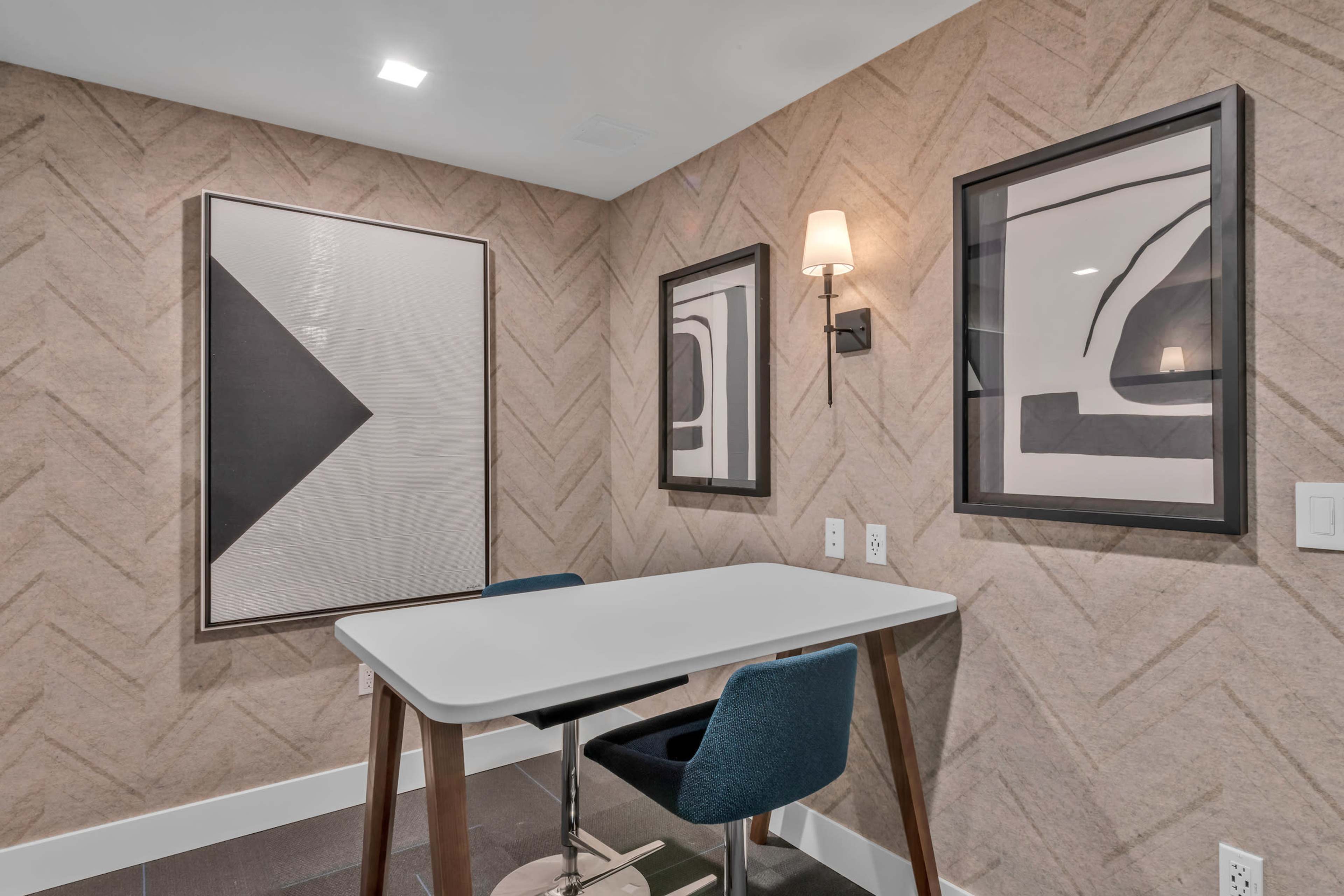 A small room featuring a table with two chairs, flanked by two framed abstract artworks on the textured wall.