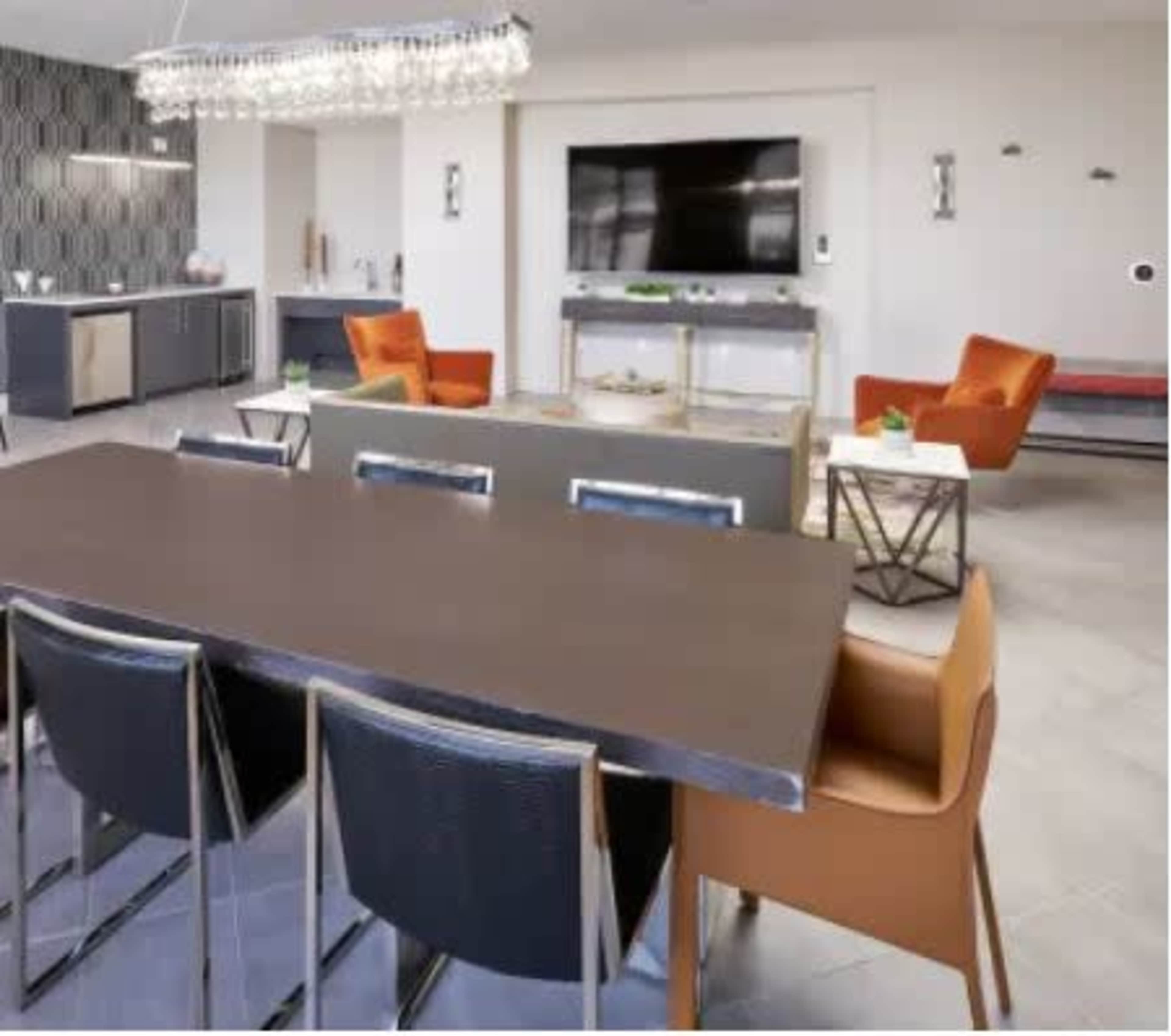 A modern dining area with a sleek table and chairs, adjacent to a living space featuring a large TV and contemporary furniture.