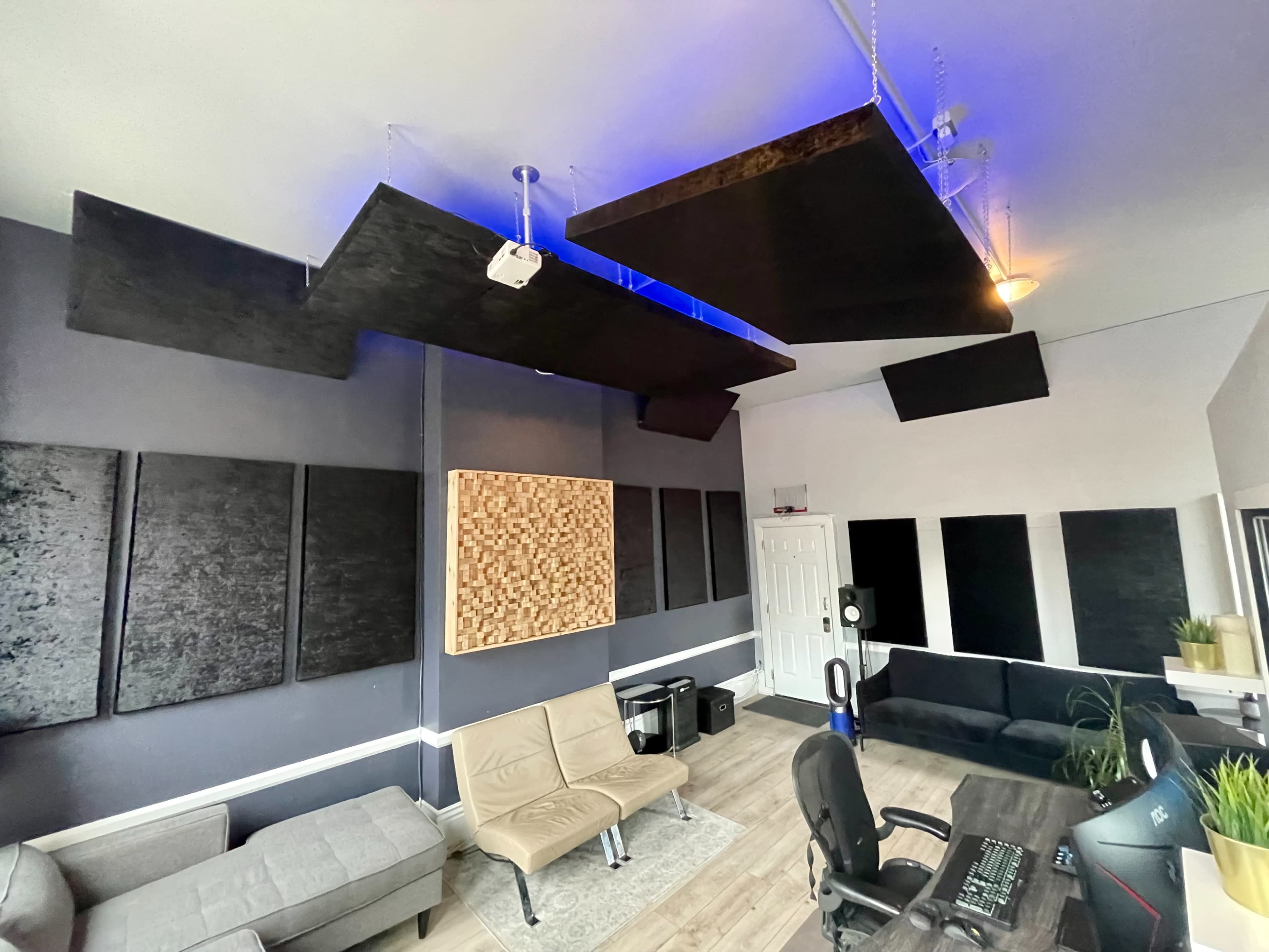 A music studio featuring soundproof panels on the walls, overhead acoustic treatments, a computer workstation, and a seating area.