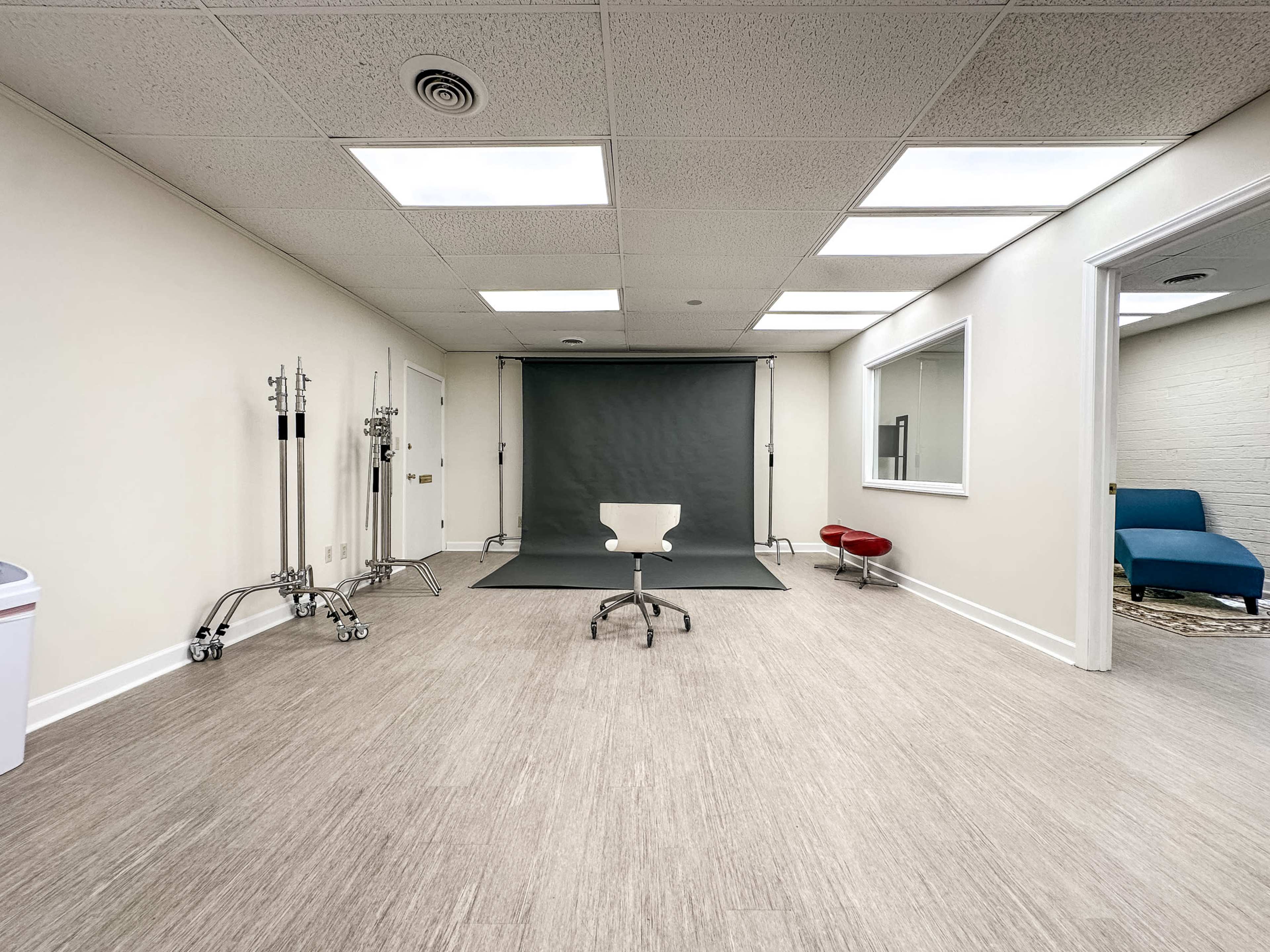 A spacious, empty photo studio featuring a chair in the center, a backdrop, and various studio equipment along the walls.