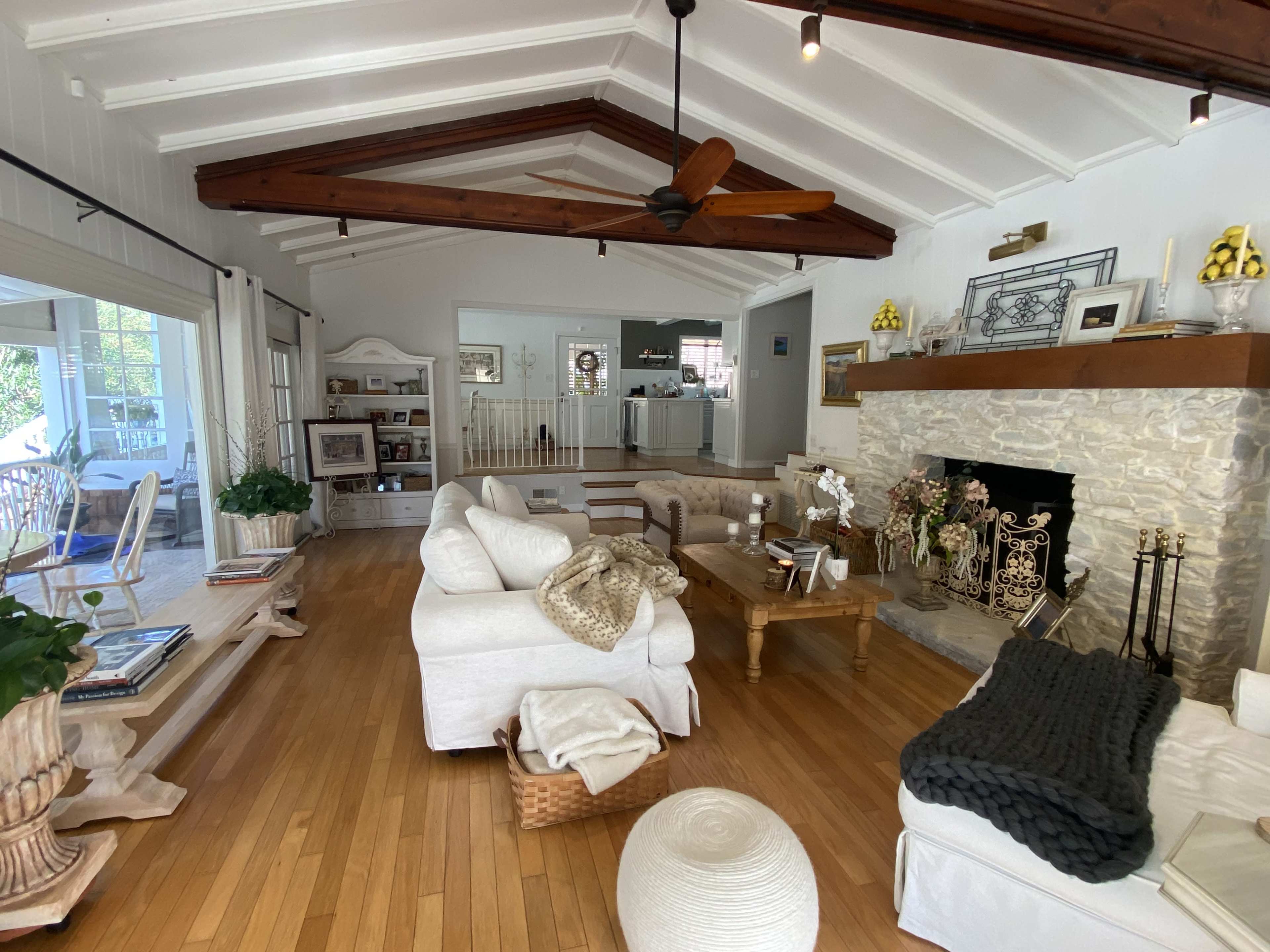 The living room features a light-colored sectional sofa, wooden furniture, and a stone fireplace beneath a vaulted ceiling with exposed beams.
