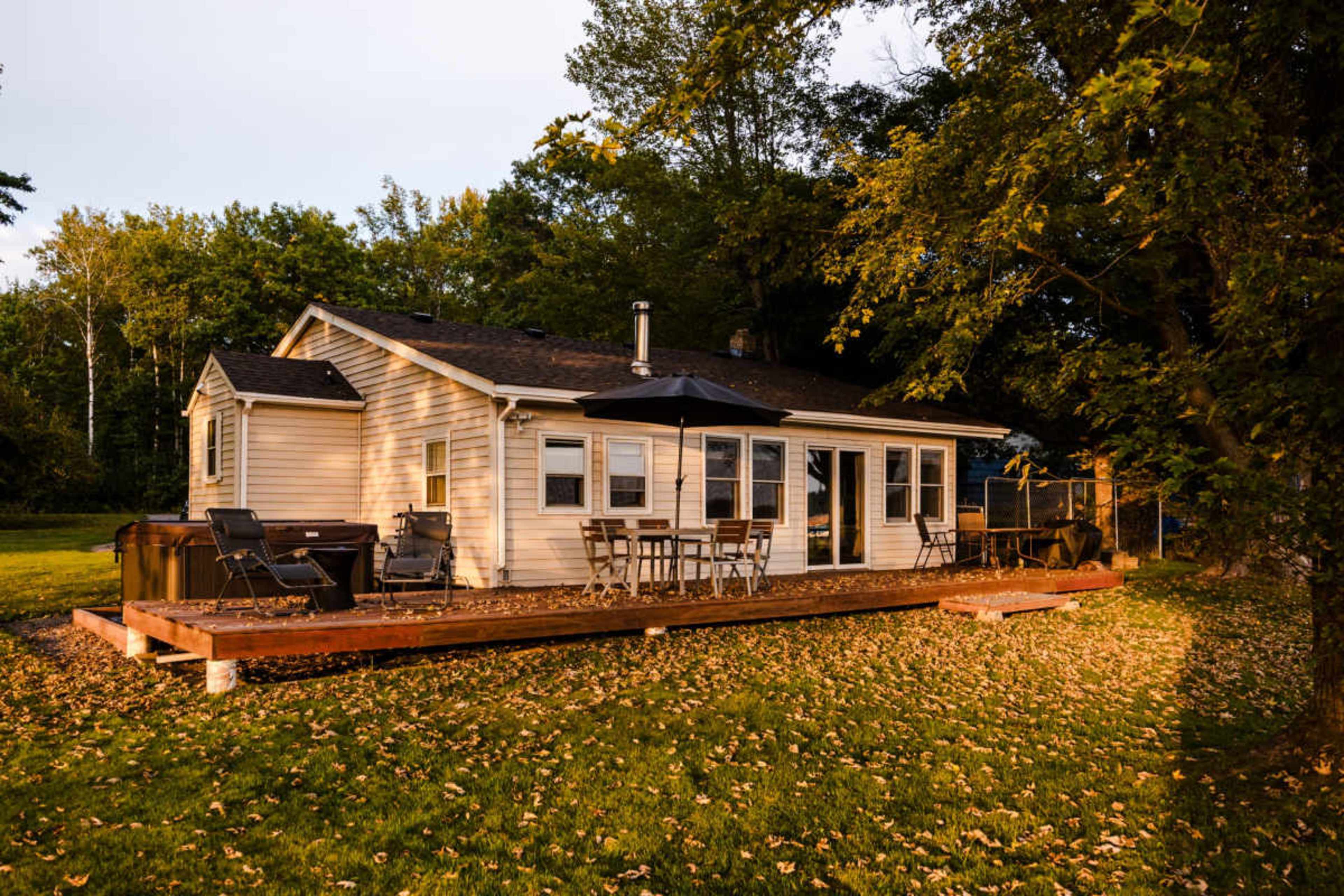 The image shows a single-story house with a wooden deck, surrounded by trees and fallen leaves.