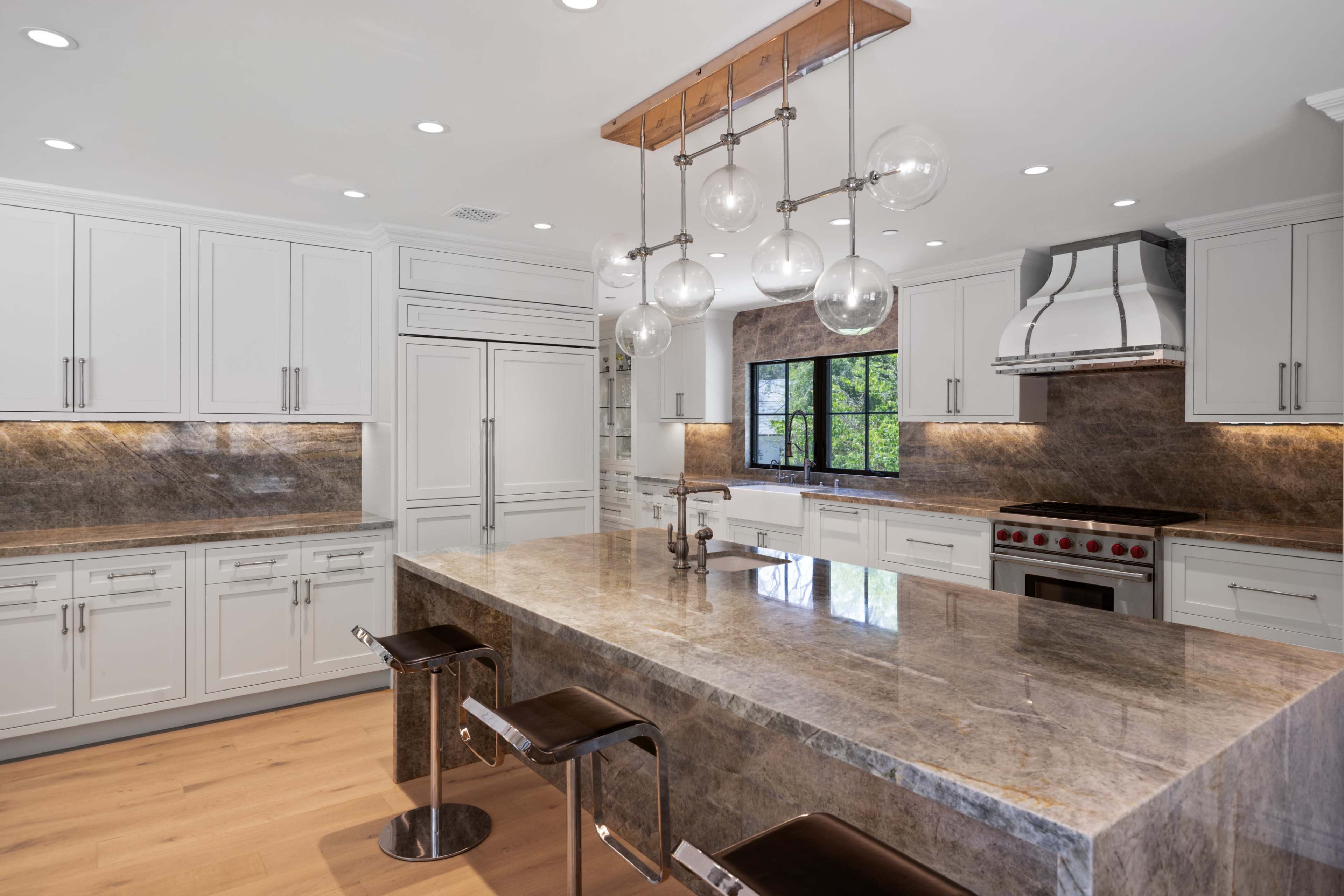The image shows a modern kitchen with white cabinetry, a large gray marble island, and pendant lighting above.