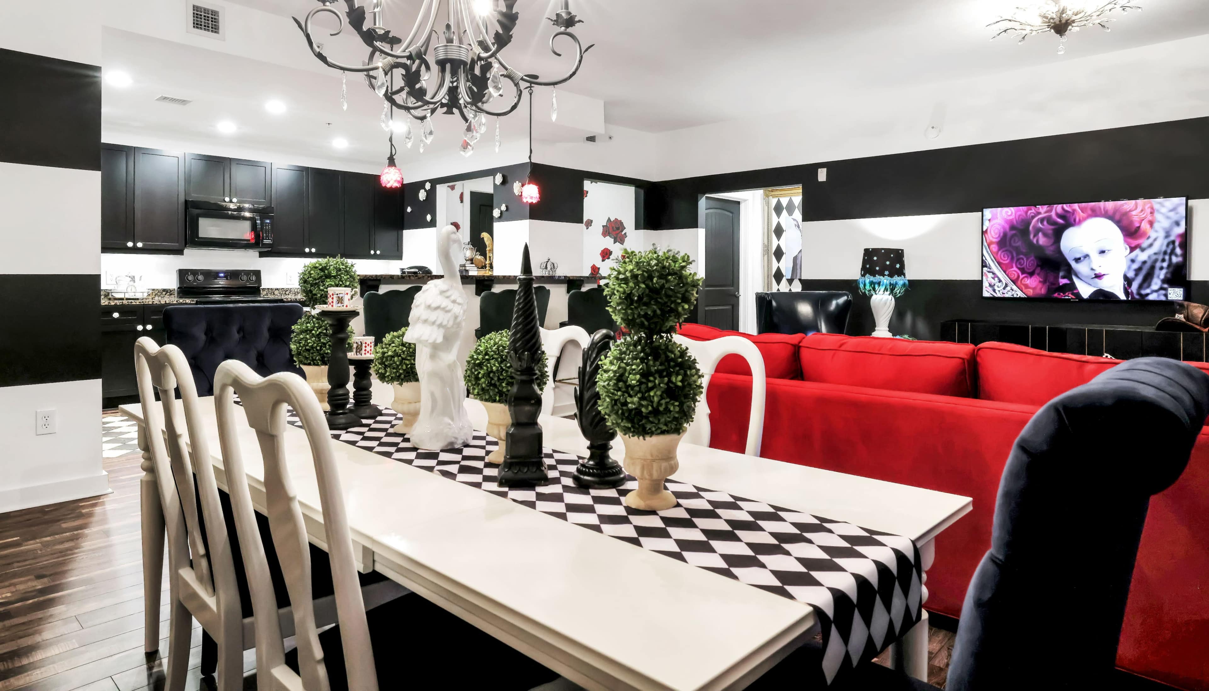 A modern living and dining area with a black and white color scheme, featuring a dining table with a checkered runner and ornamental greenery, and a red sofa arranged in the space.