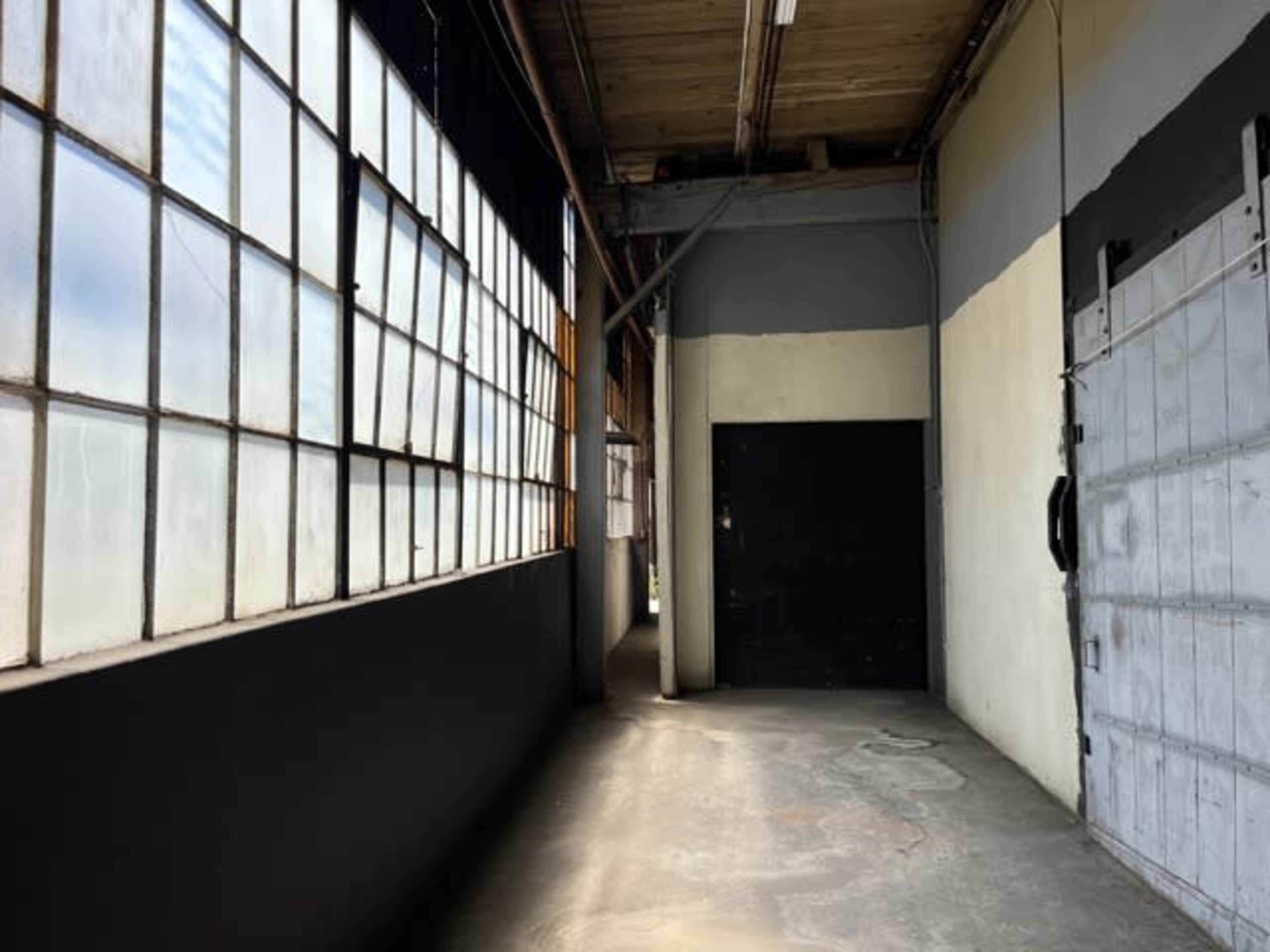 A narrow corridor with large windows on one side and a black door at the end.
