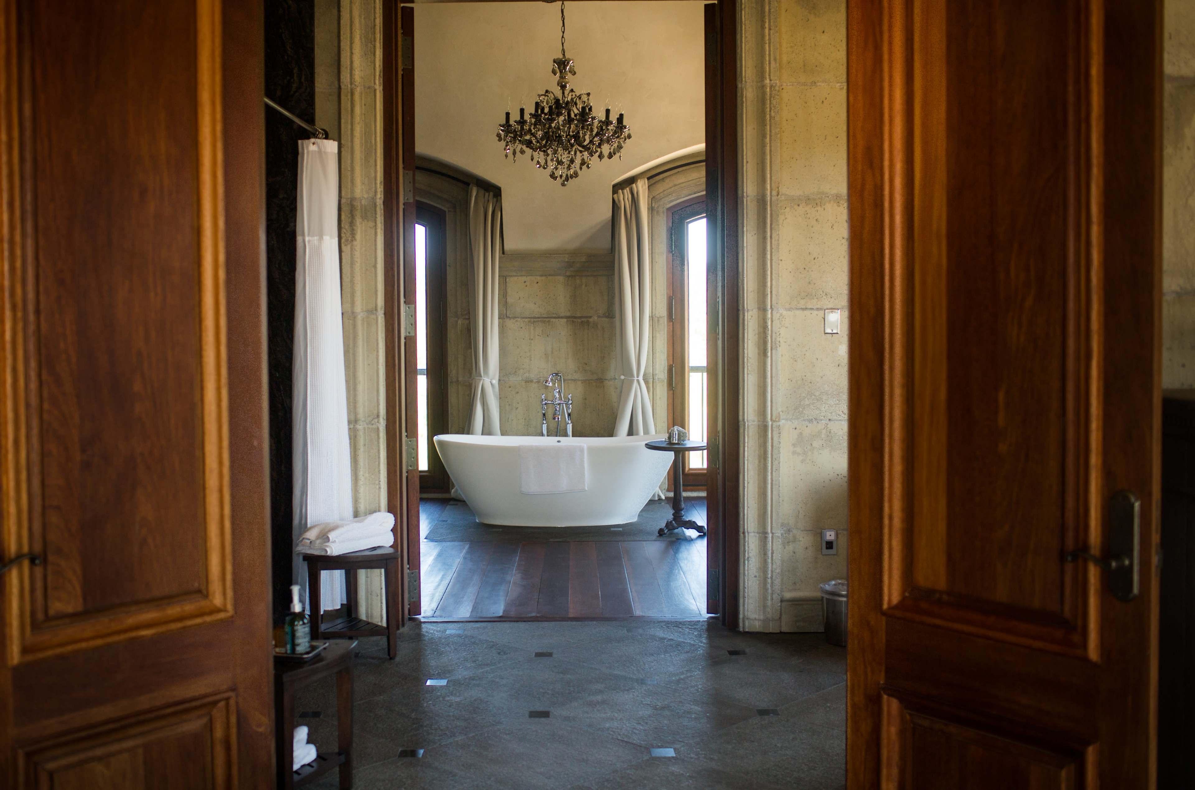 A spacious bathroom features a freestanding bathtub and large windows, framed by elegant curtains.