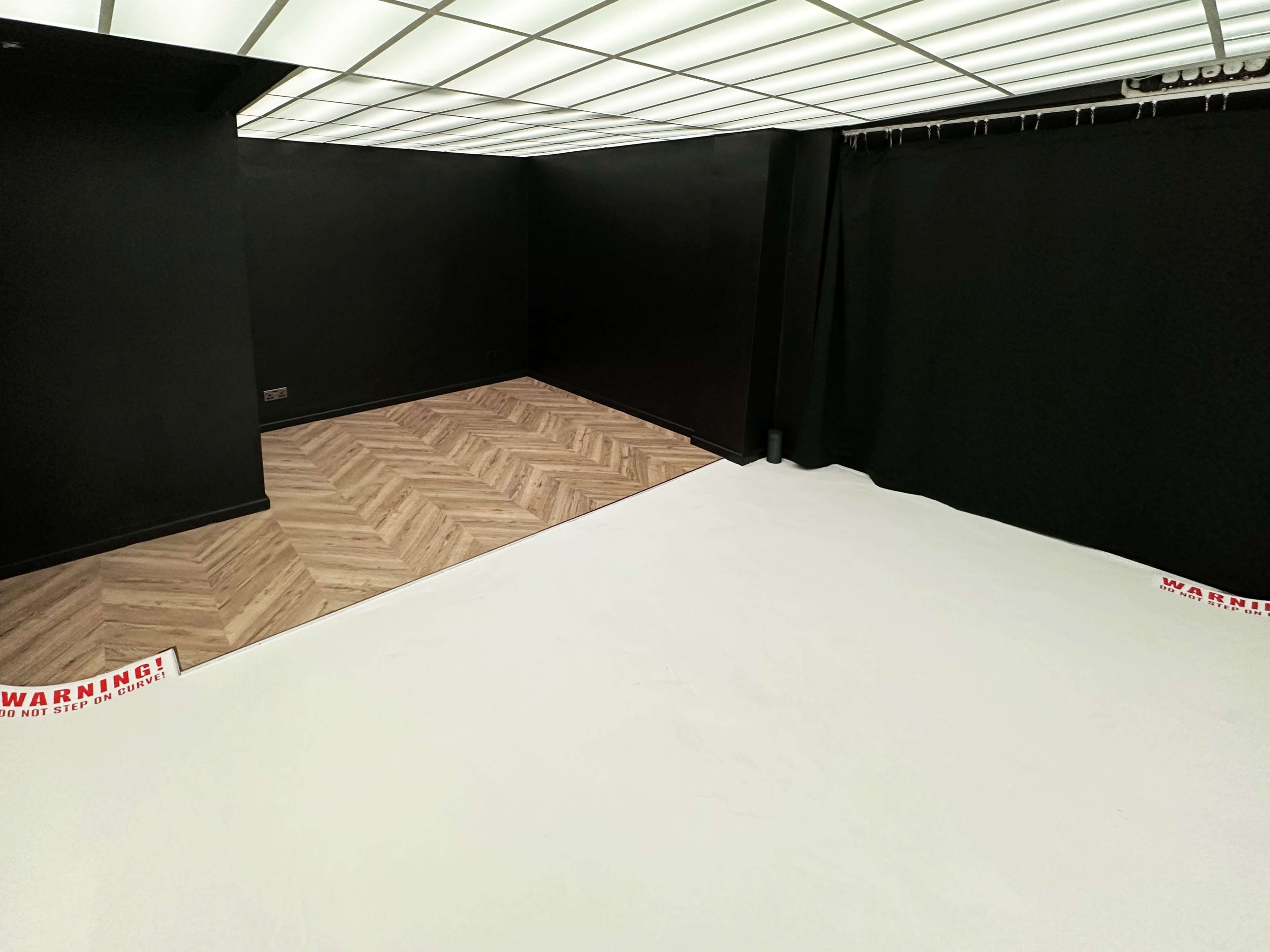 A room with black walls and a mix of wood and white flooring, featuring a warning sign on the ground.