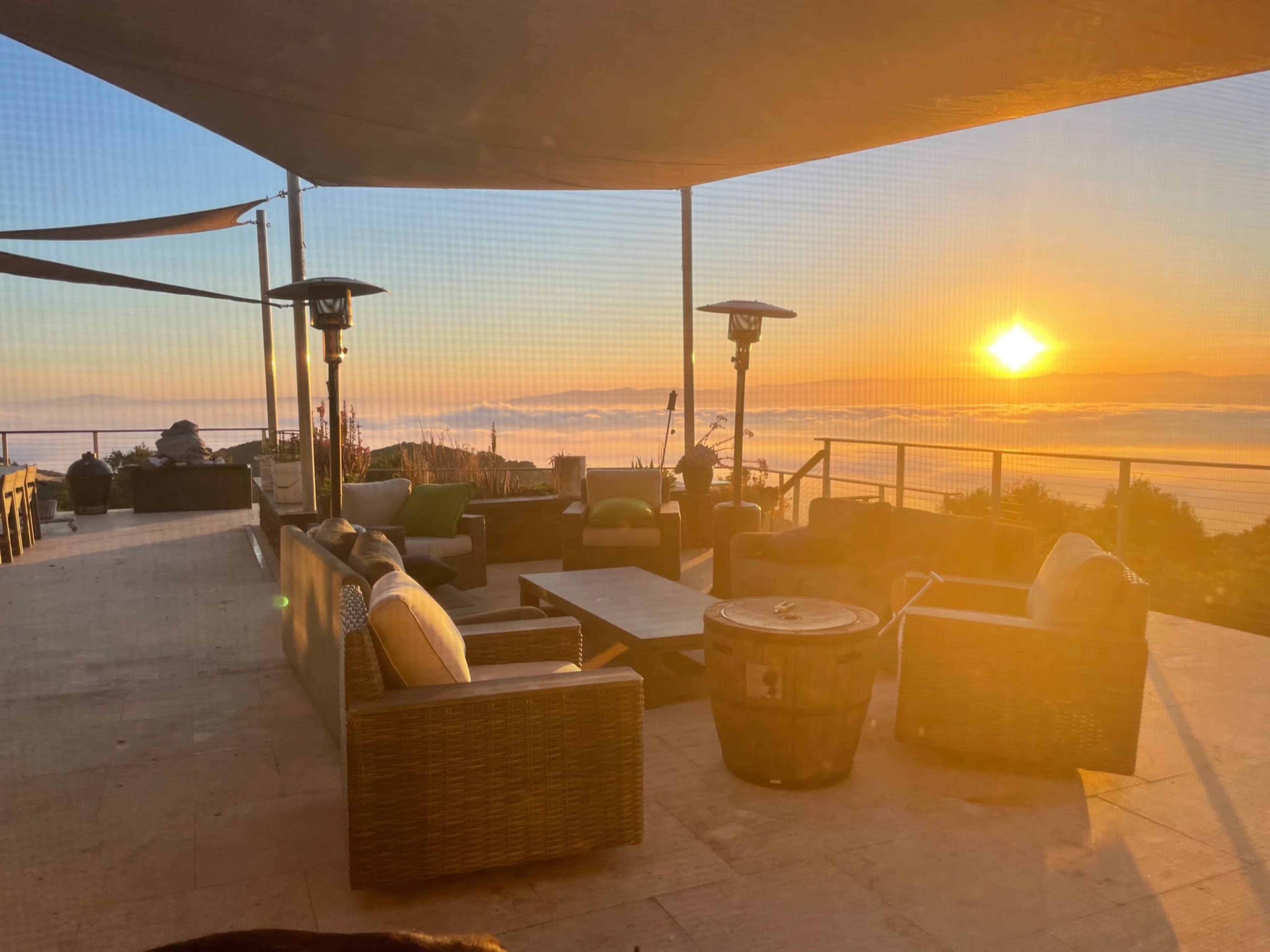 A patio with outdoor seating overlooks a sunset above a fog-covered landscape.