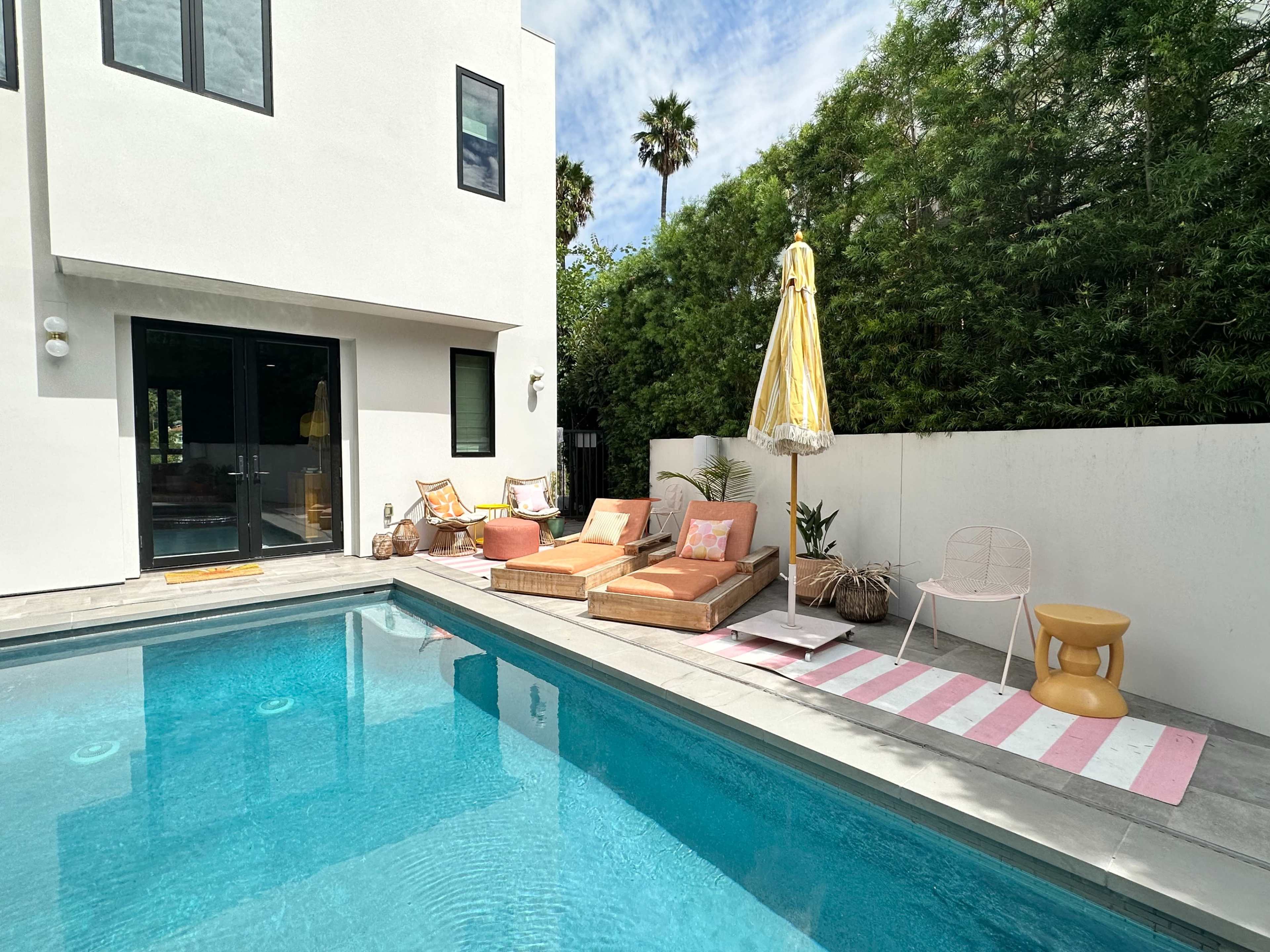 A modern backyard with a swimming pool, lounge chairs, an umbrella, and decorative plants.