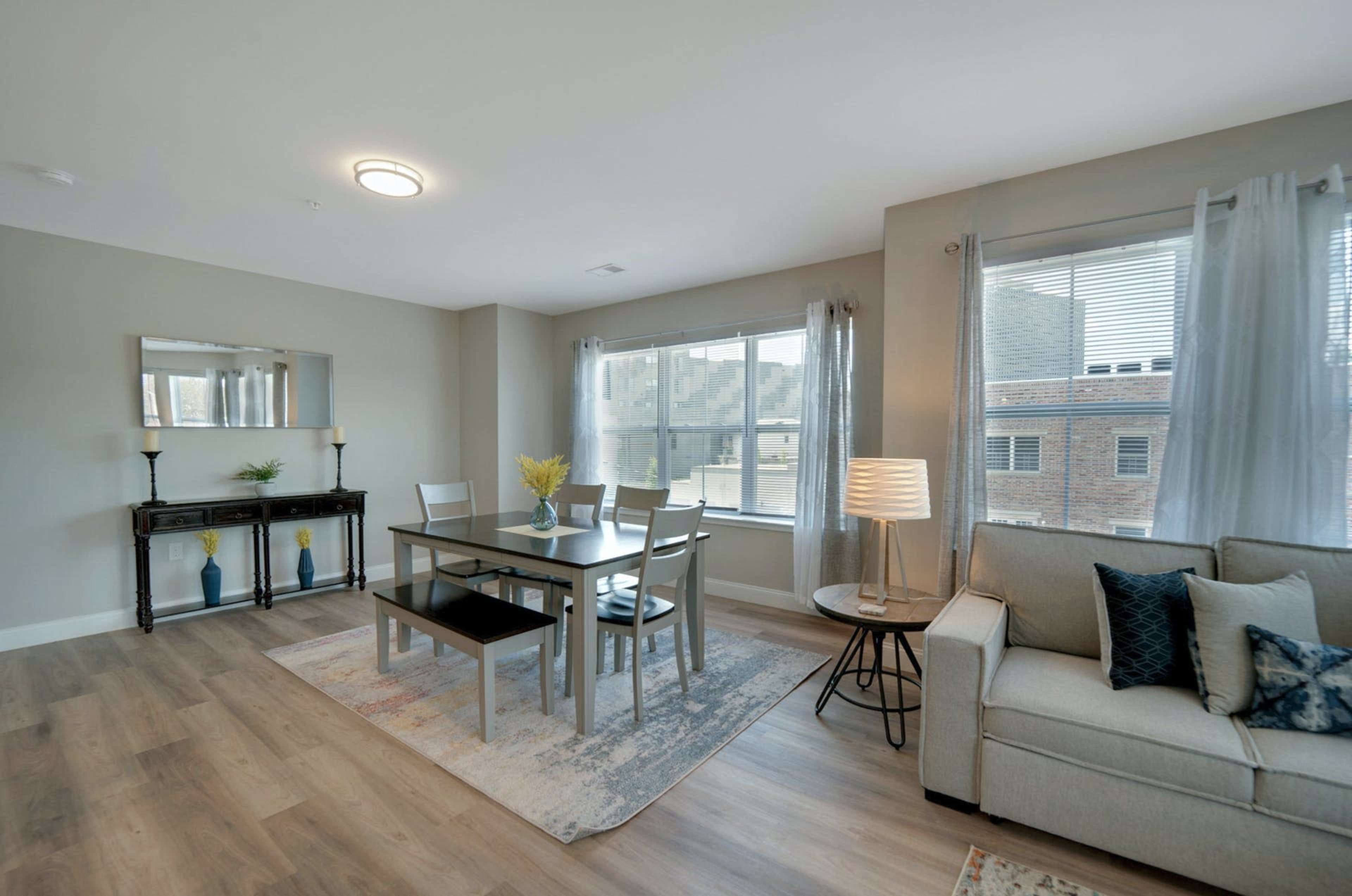 A modern living space featuring a dining area with a table and chairs, a couch, and large windows allowing natural light to enter.