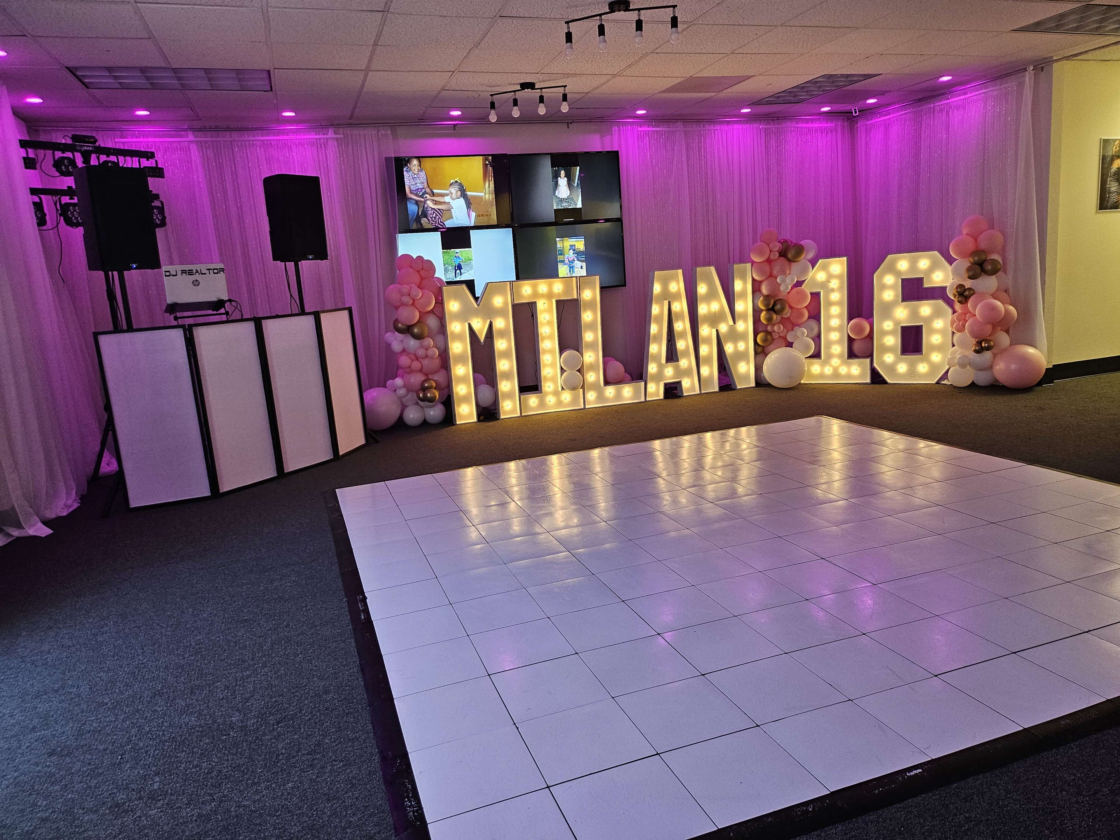 The scene features a decorated event space with large illuminated letters spelling "MILAN 16," a dance floor, and colorful balloons arranged nearby.